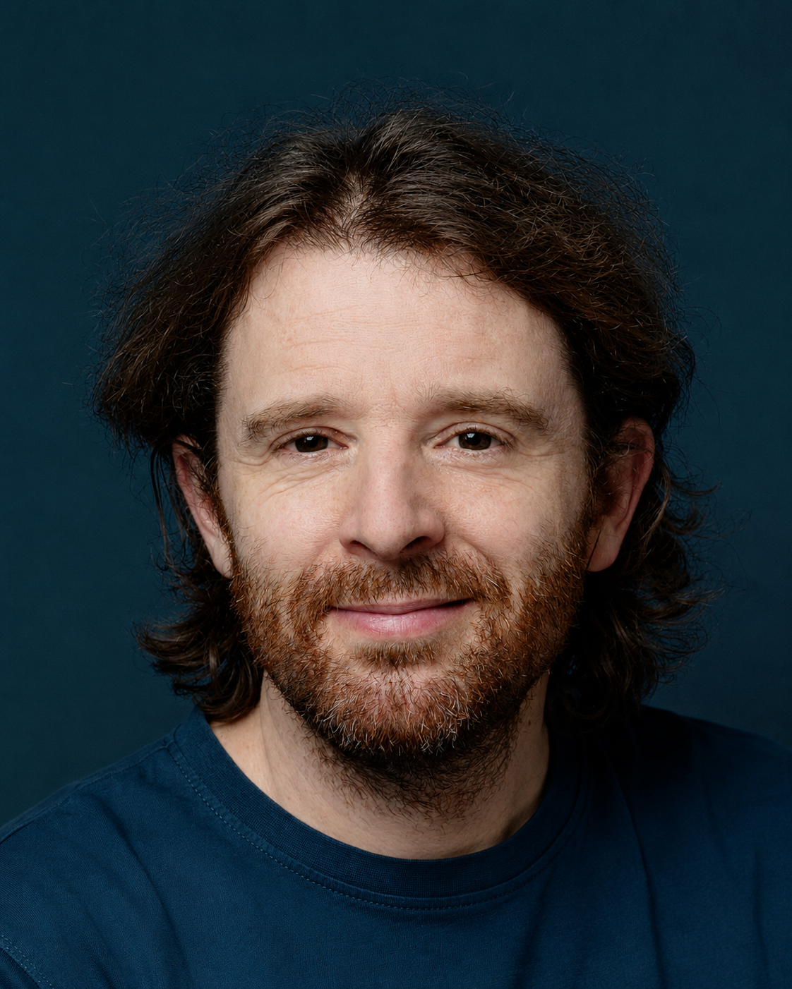 Portrait eines lächelnden Mannes mit mittellangen braunen Haaren