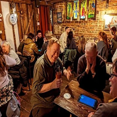 People socializing and drinking in a cozy restaurant with brick walls, colorful artwork, and warm lighting.