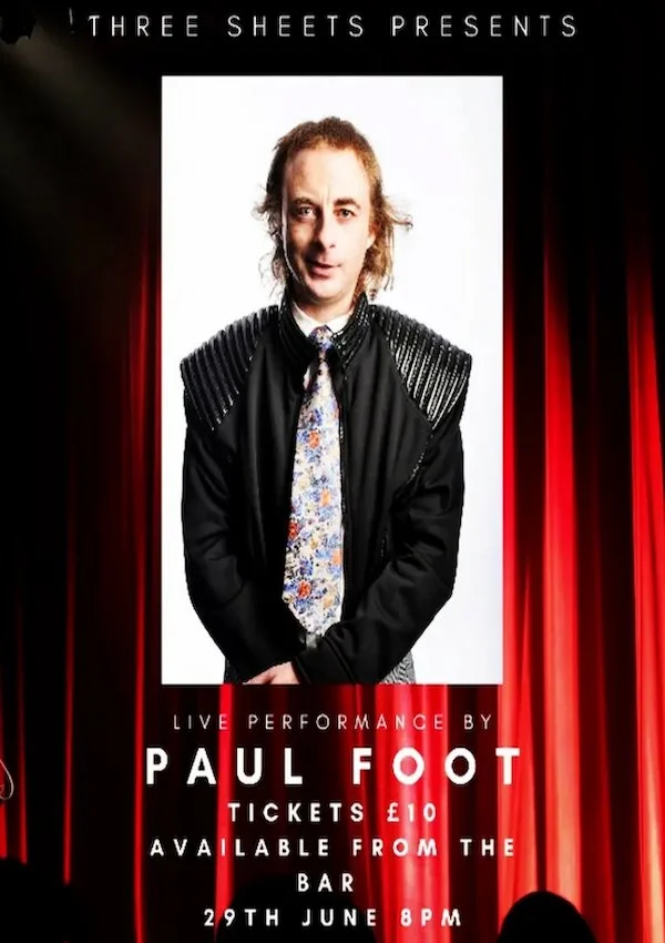 Poster advertising a live performance by Paul Foot on June 29th at 8 PM. The poster features a photo of Paul Foot, a man with shoulder-length hair, wearing a black jacket with shoulder details, a patterned shirt, and a colorful tie. The background ha