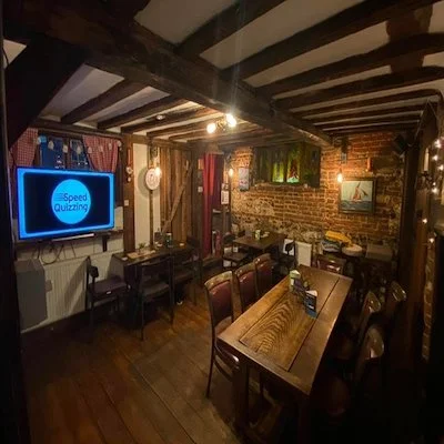 Interior of a cozy pub or restaurant with wooden beams, brick walls, a mounted TV, and wooden tables and chairs.