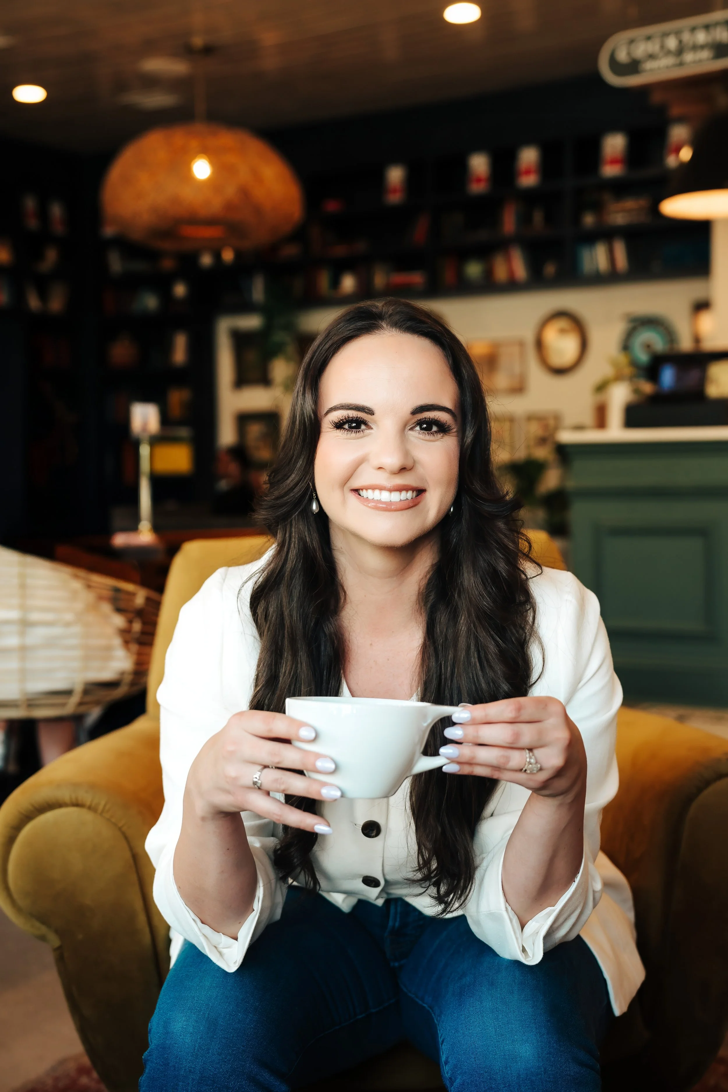 Woman smiling on a couch holding a cup at a coffee shop