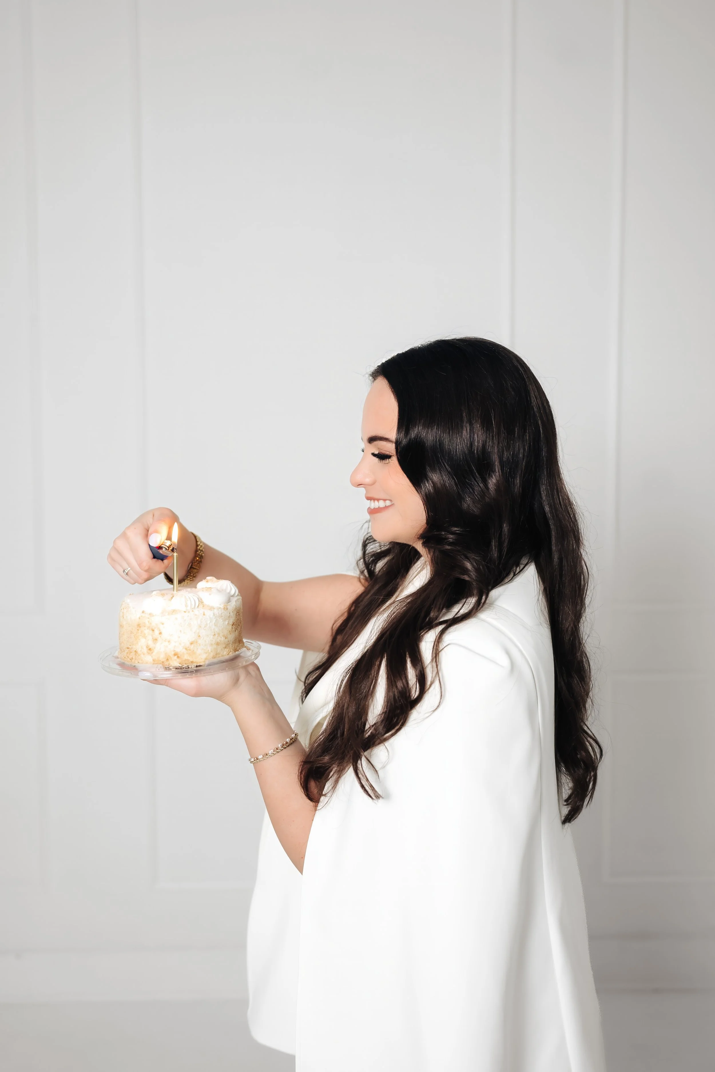 Smiling woman in white cake lights candle on a mini birthday cake