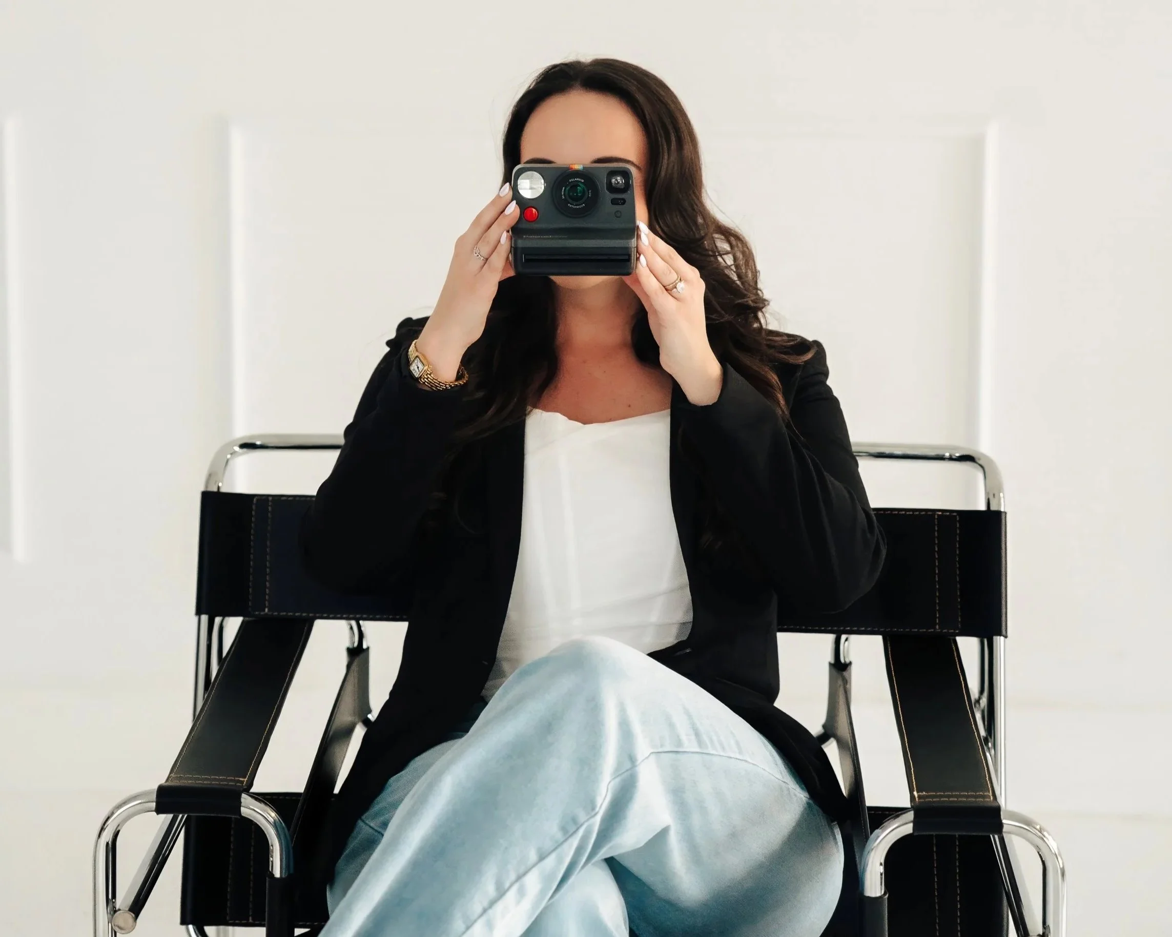 Image of a woman sitting in a chair and holding a polaroid camera