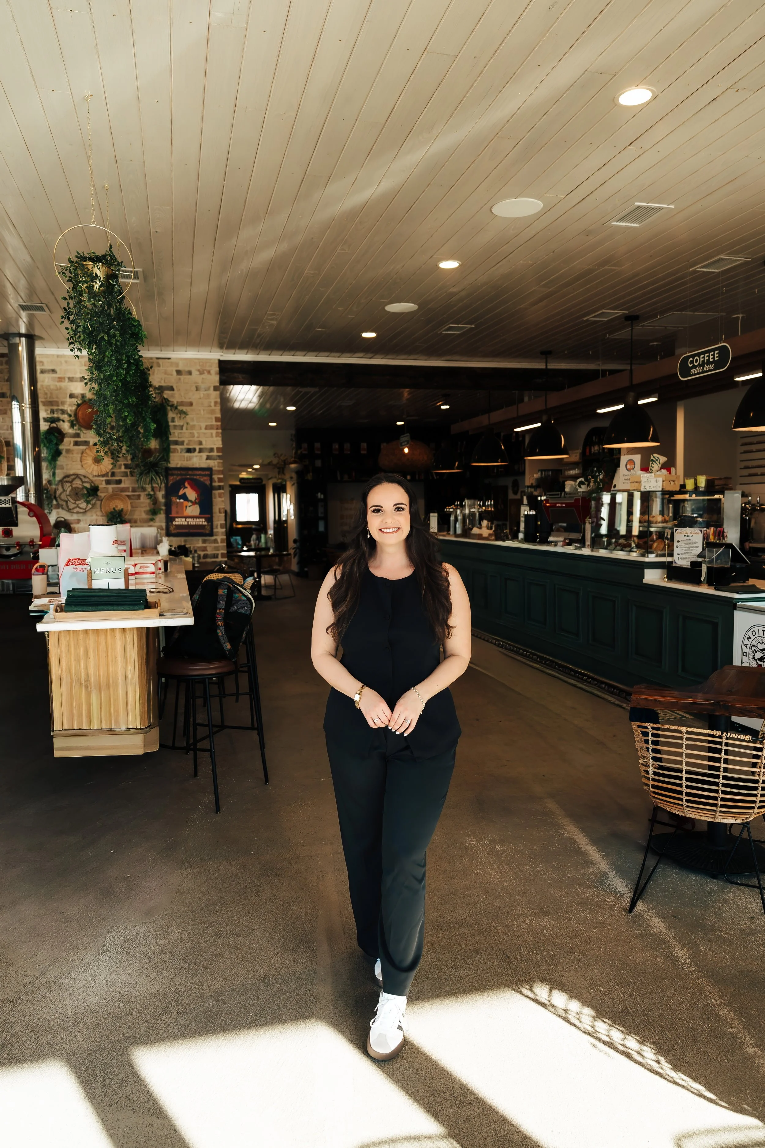 Woman wears black jumpsuit in the middle of empty coffeeshop