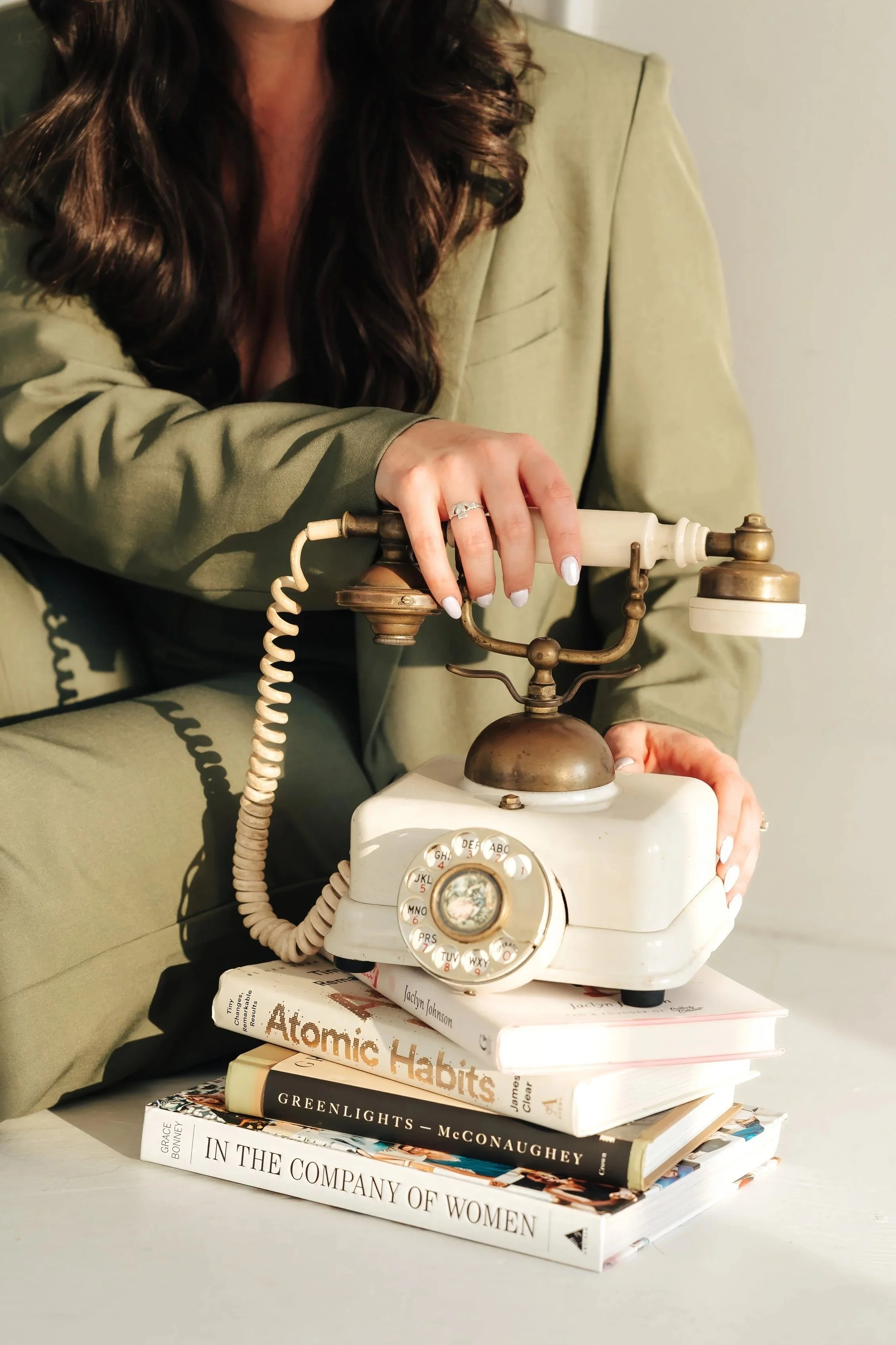 Abstract image of a woman in a green suit holding a rotary phone on a pile of books