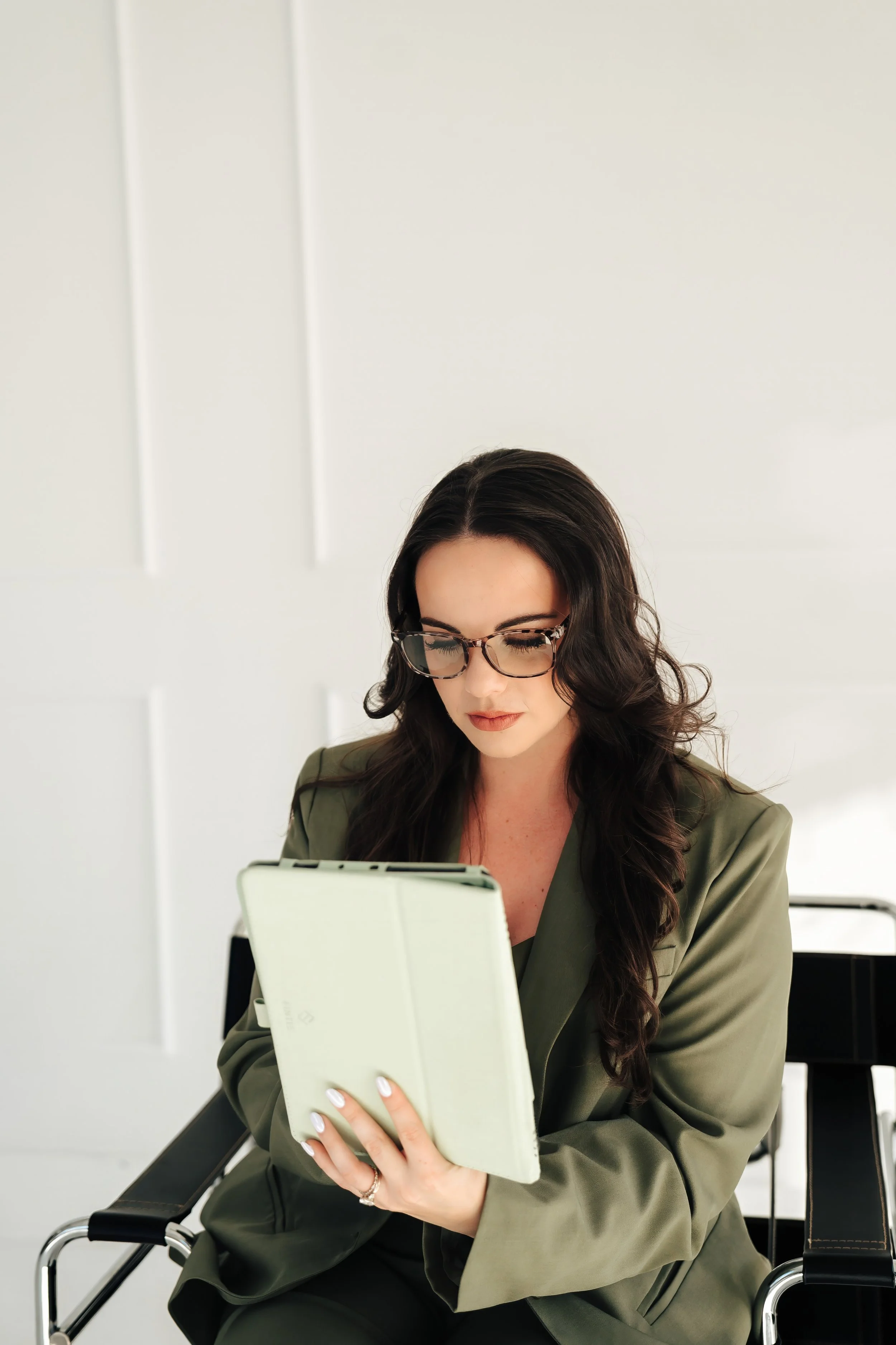 Serious woman in glasses wearing a green suit and holding a tablet