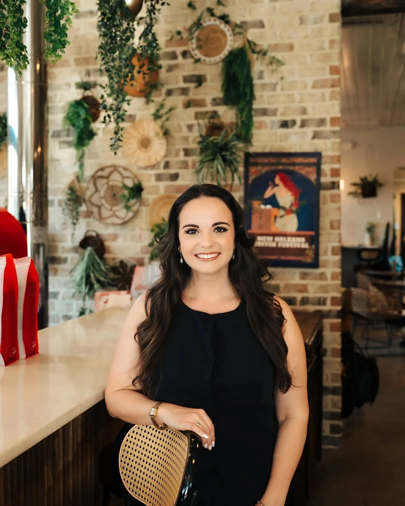 Smiling woman in black jumpsuit leans against a barstool at a coffeeshop