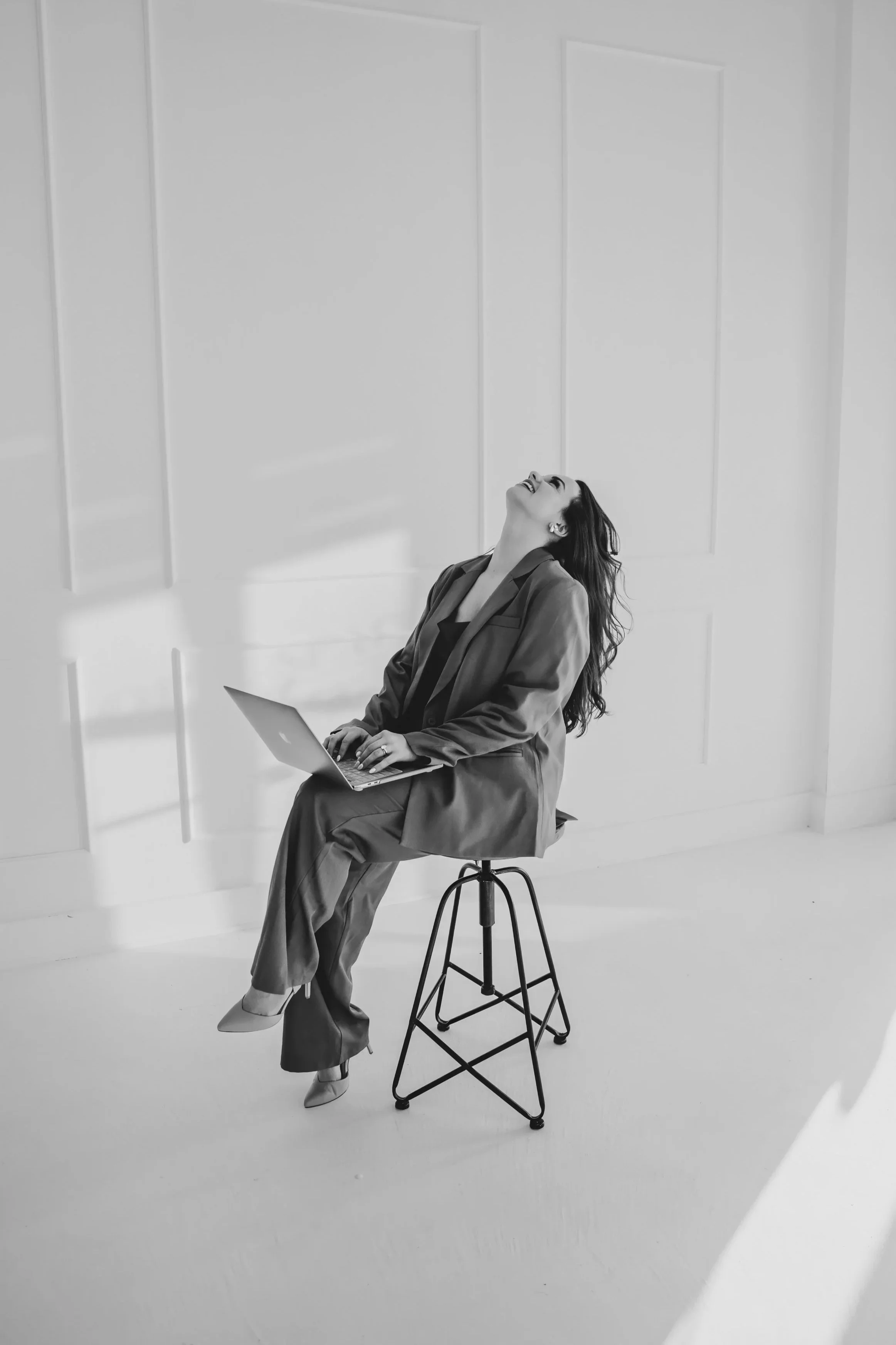 Woman laughing on a stool holding a laptop