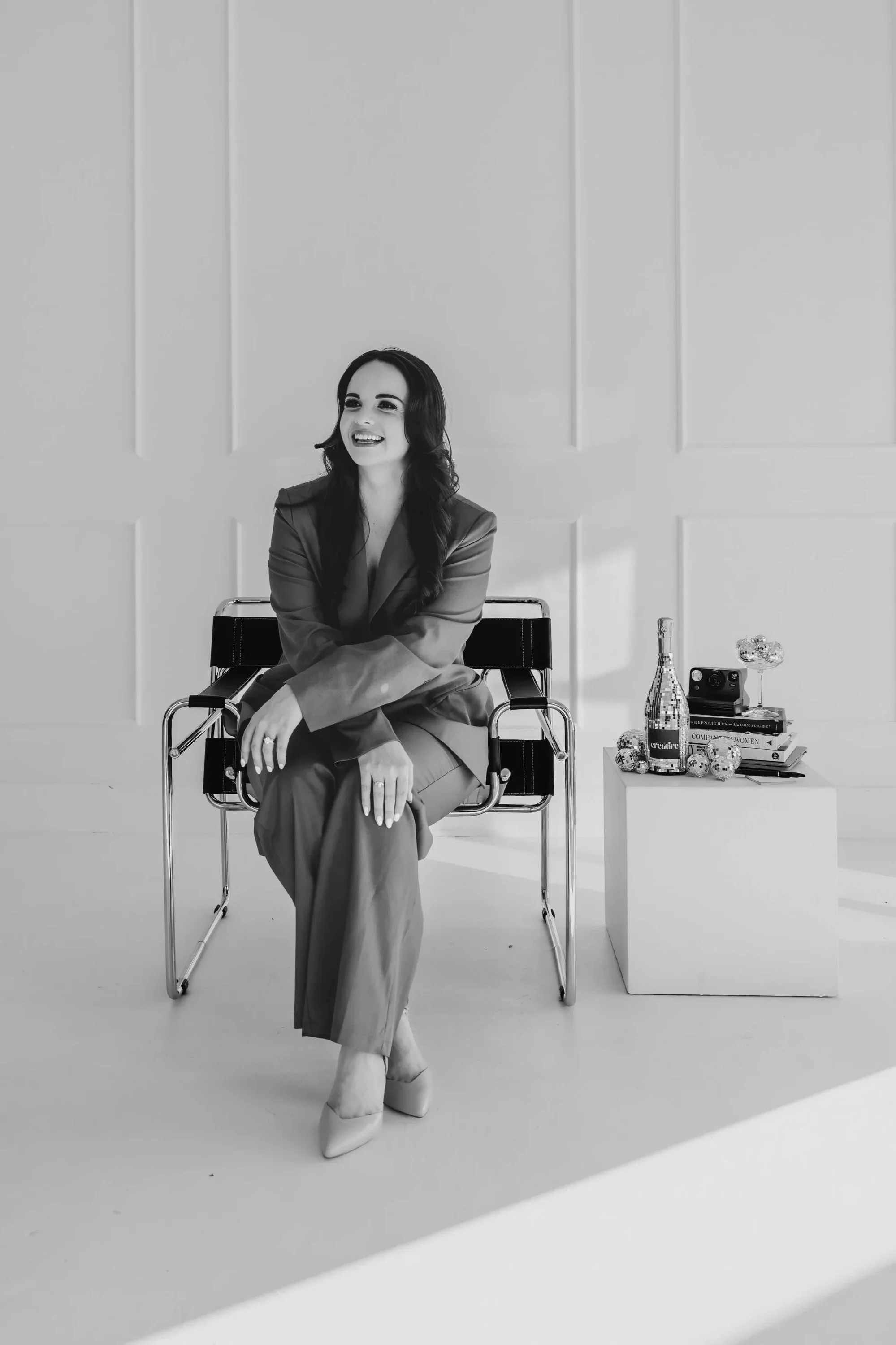 Black and white image of smiling woman sitting on a chair with props next to her
