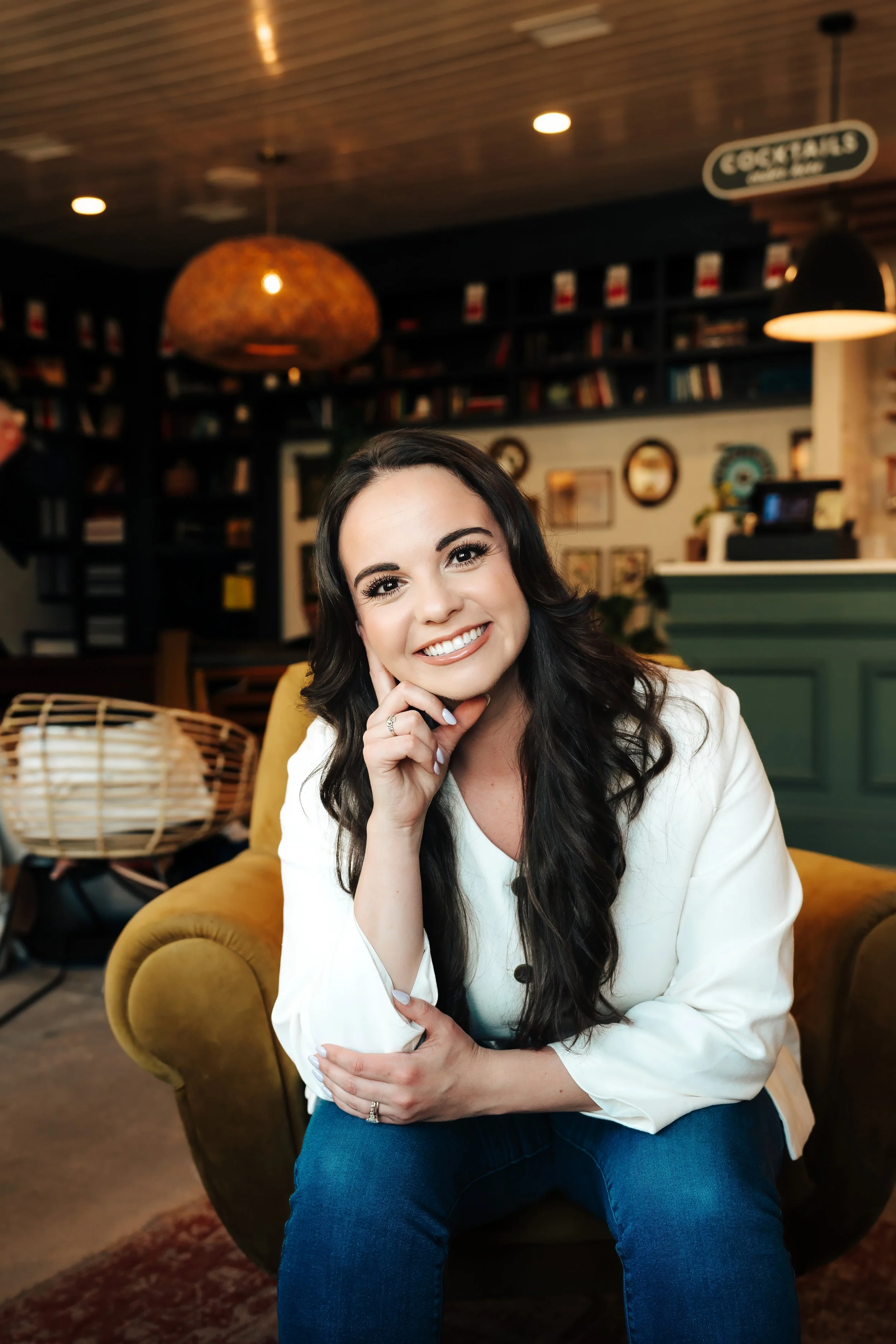 Woman leans her chin on her hand, smiling in front of bookcases