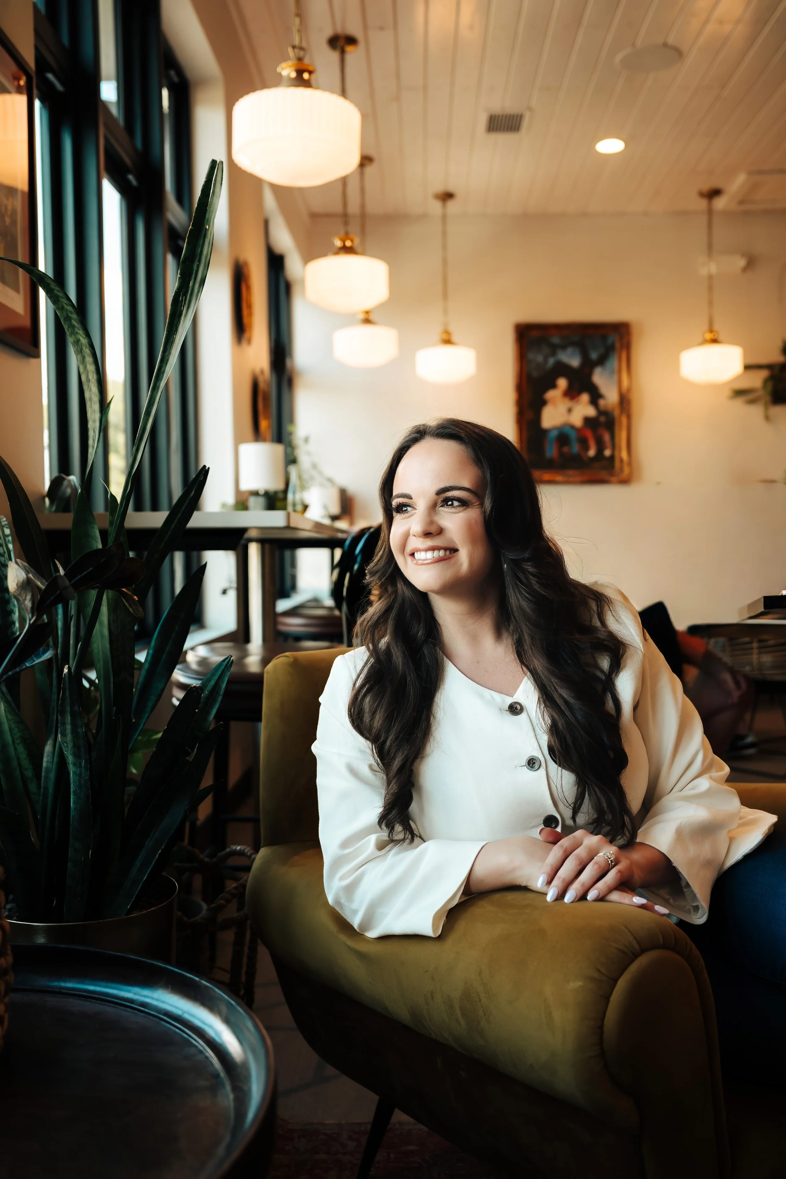 Woman smiles off camera while sitting on a couch at a bright coffeeshop