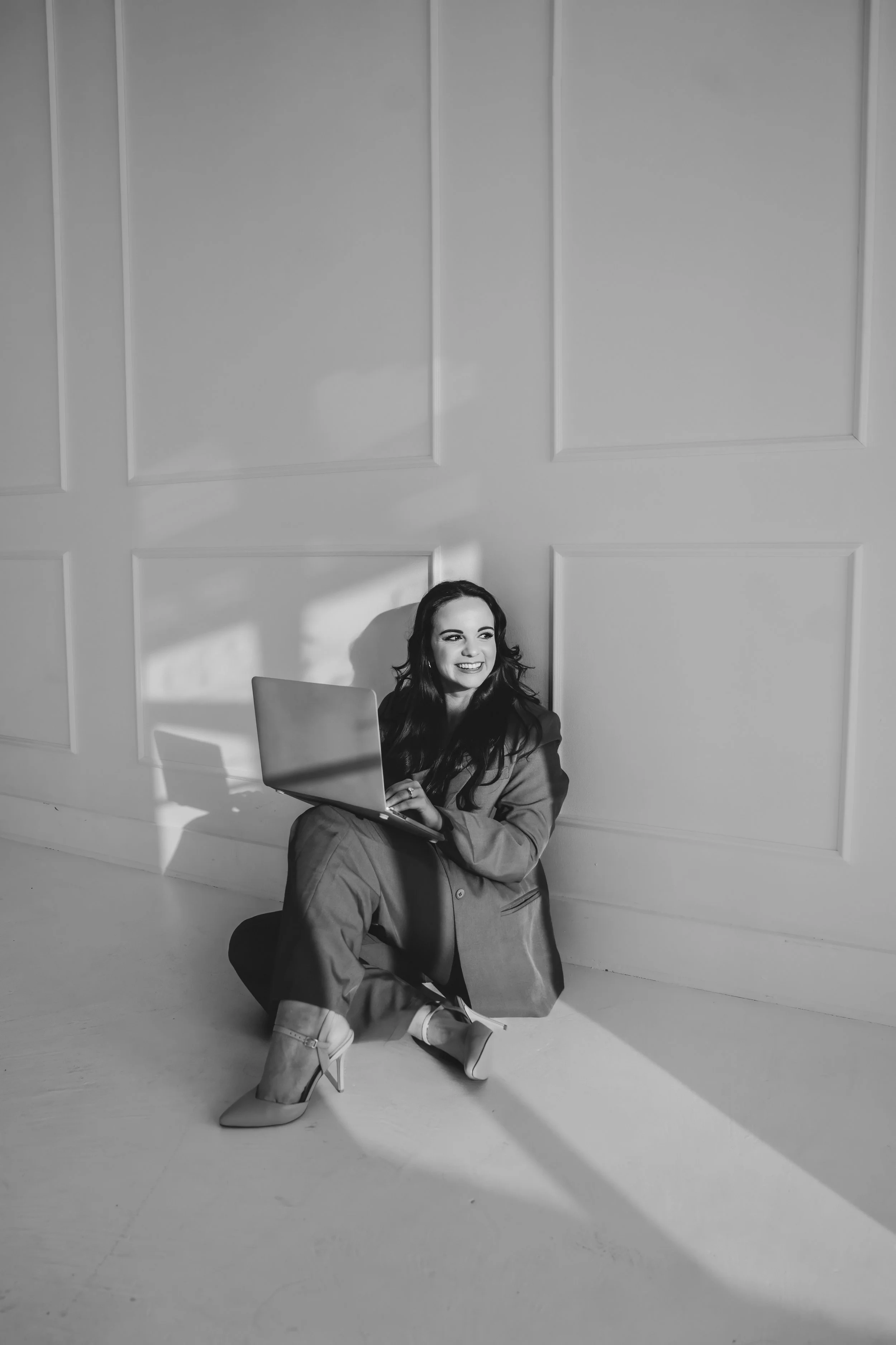 Woman leaning against a wall smiling and holding a laptop in her lap