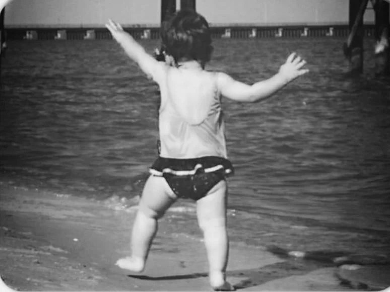 Black and white photo of a baby running on a beach