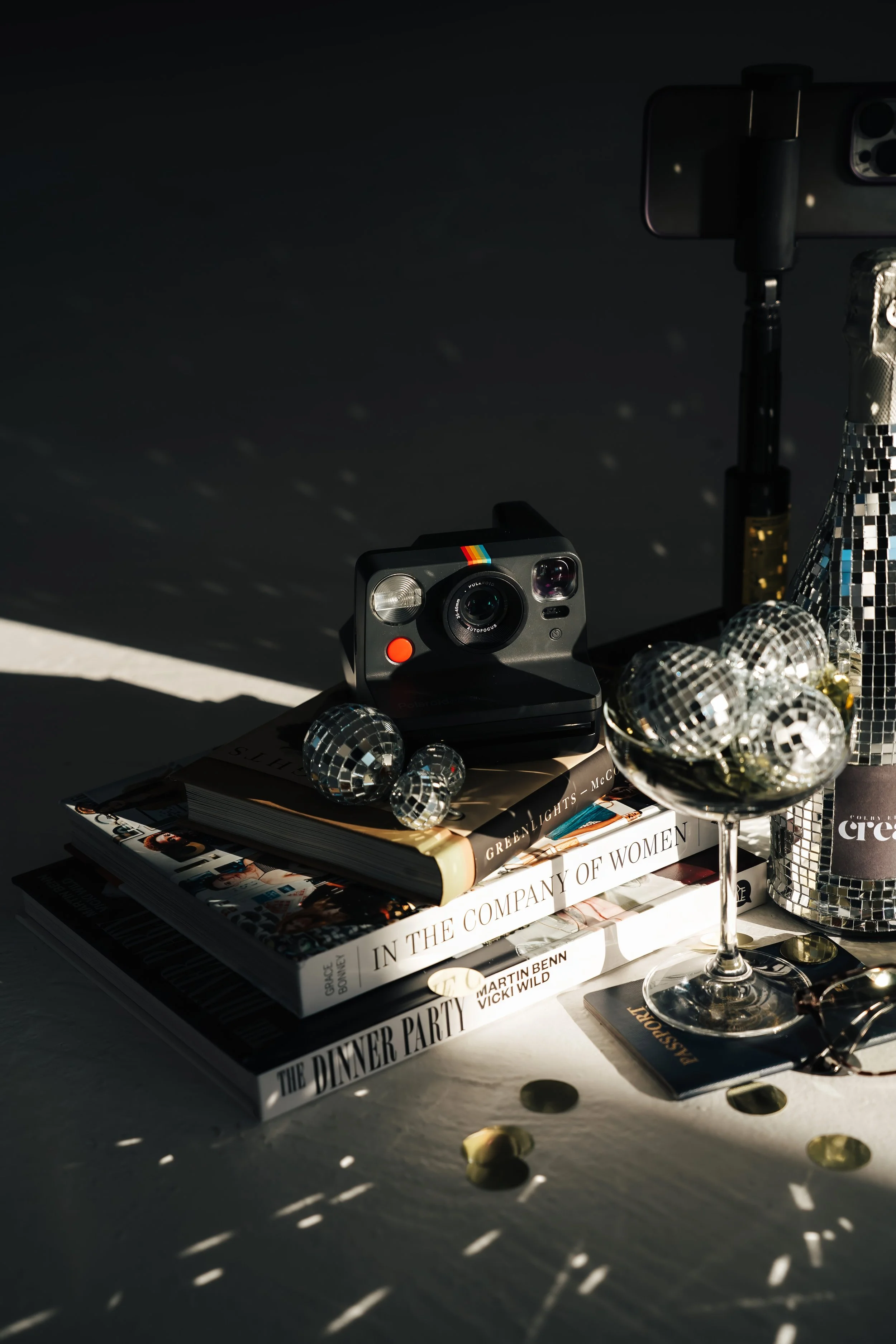 A polaroid camera on a stack of books next to a champagne glass filled with disco balls