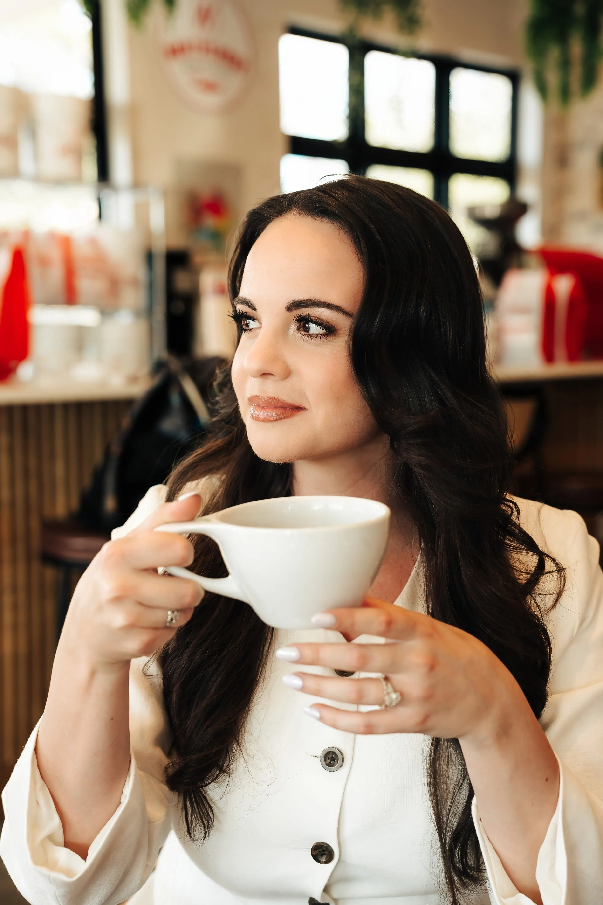 Woman in white button jacket holds a coffee cup at a shop