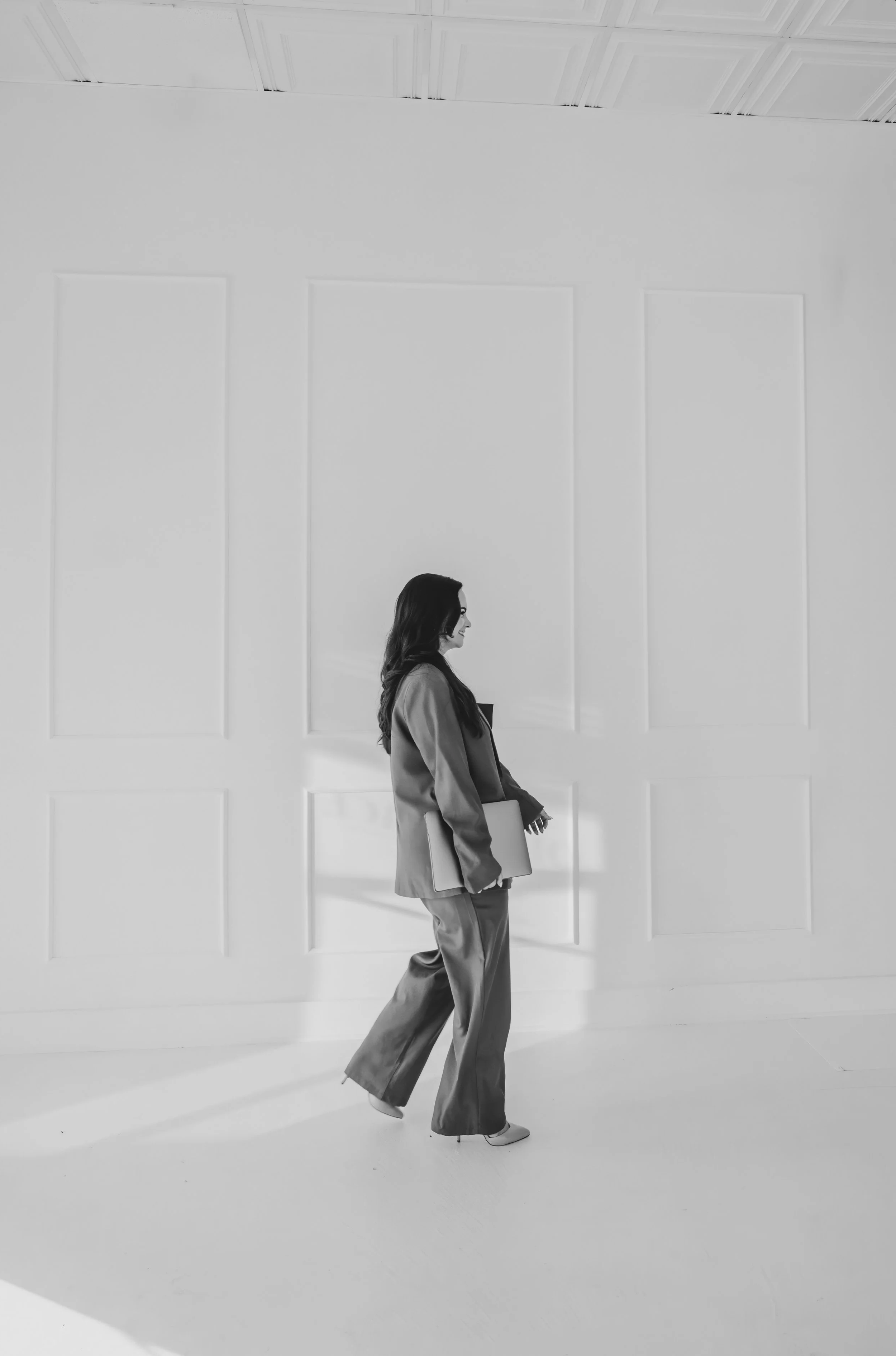 Black and white image of woman walking in suit holding a laptop