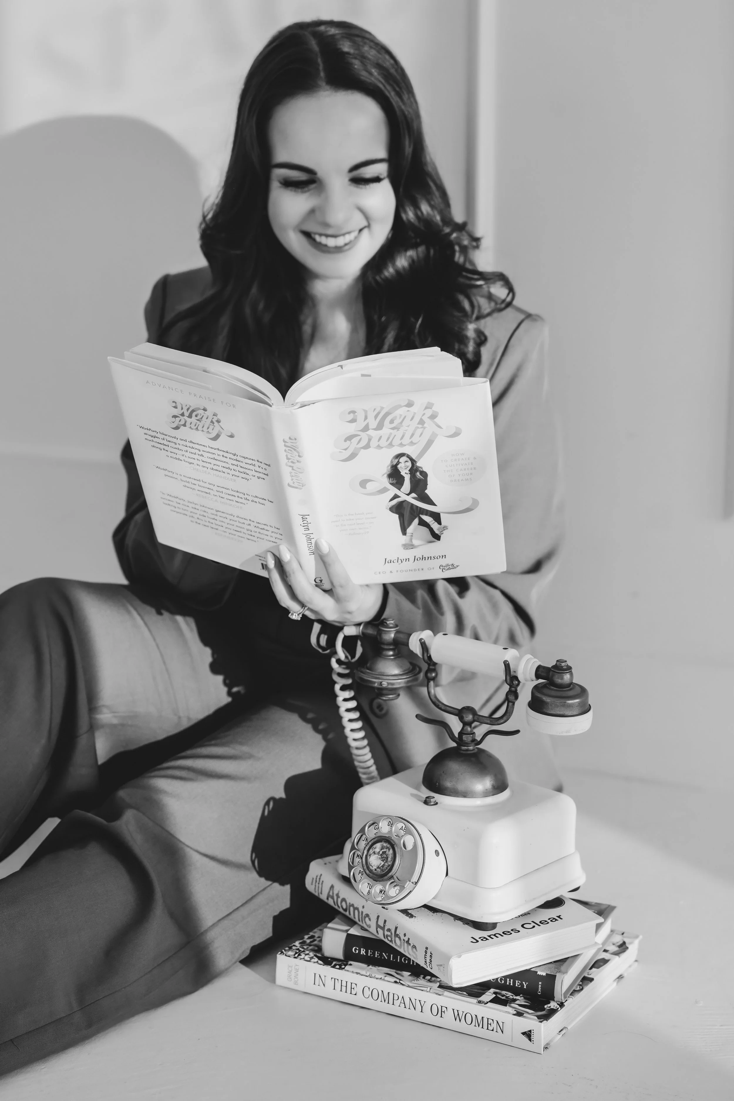 Smiling woman holds a rotary phone and reads the book Work Party by Jaclyn Johnson