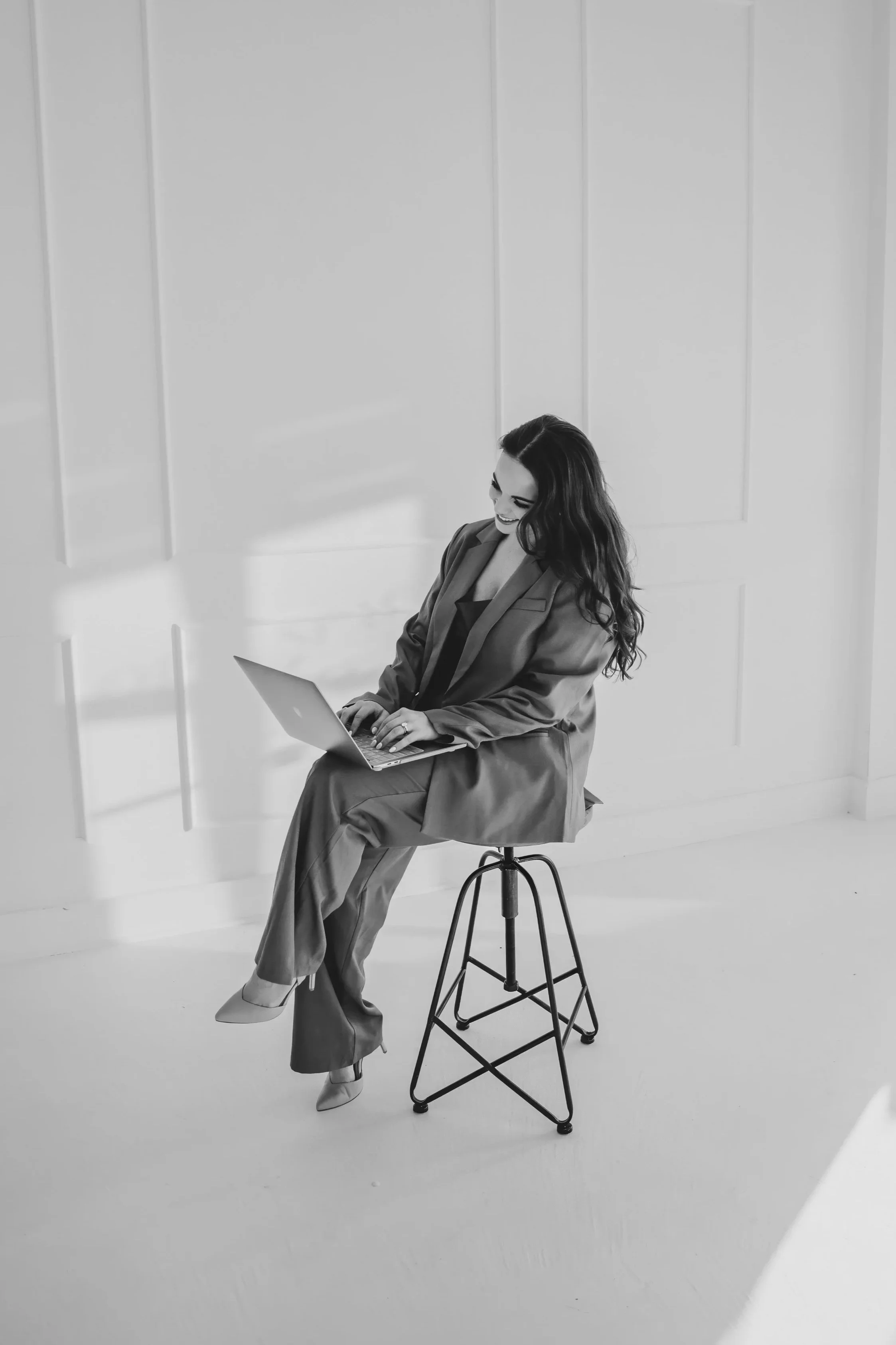 Woman sitting on stool smiling with laptop