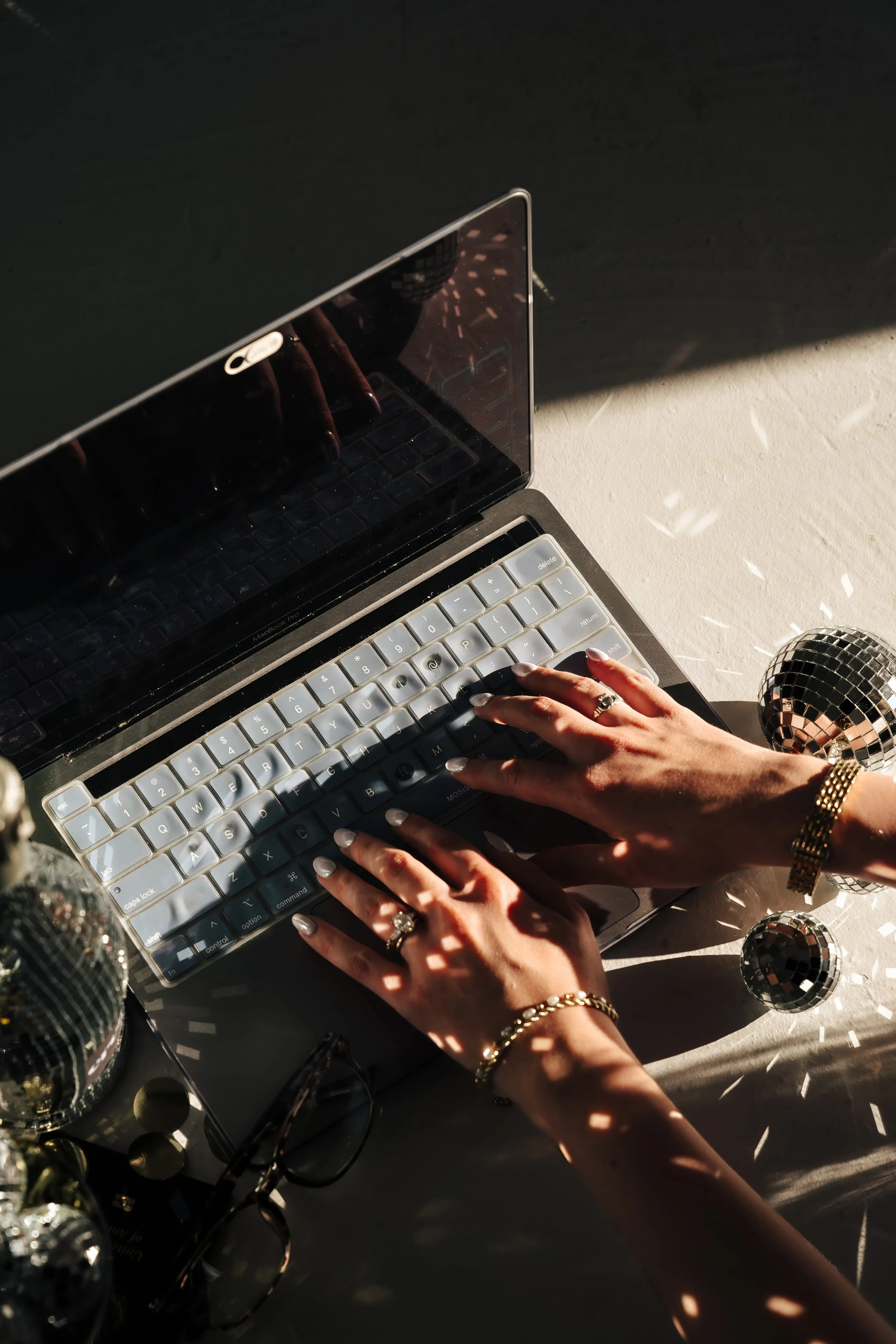Woman types on gray laptop keyboard with disco balls