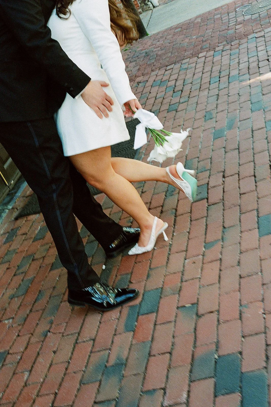 Candid, faceless image of a couple's legs on their wedding day with a bouquet