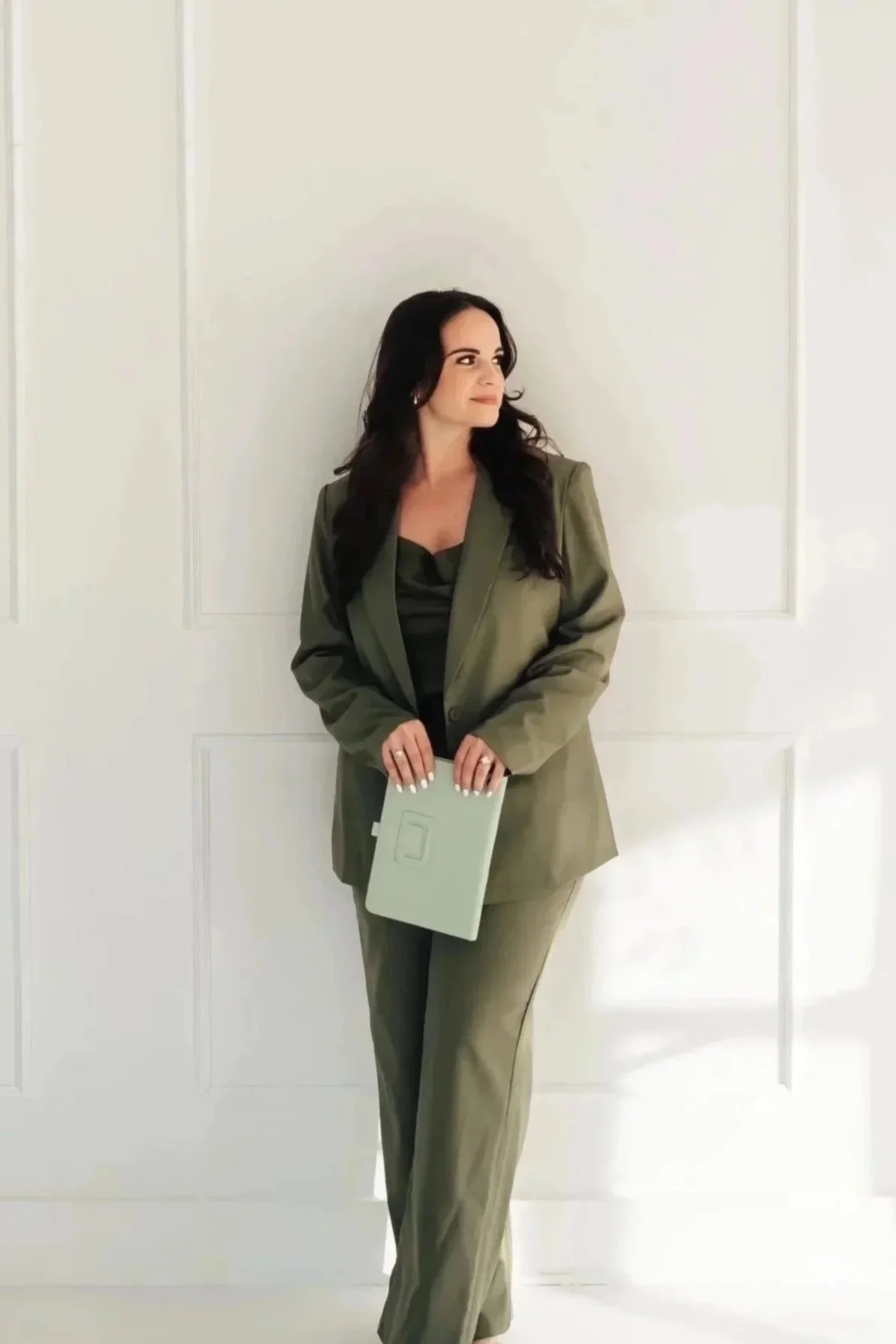 Woman in a green suit leaning against a wall holding a tablet