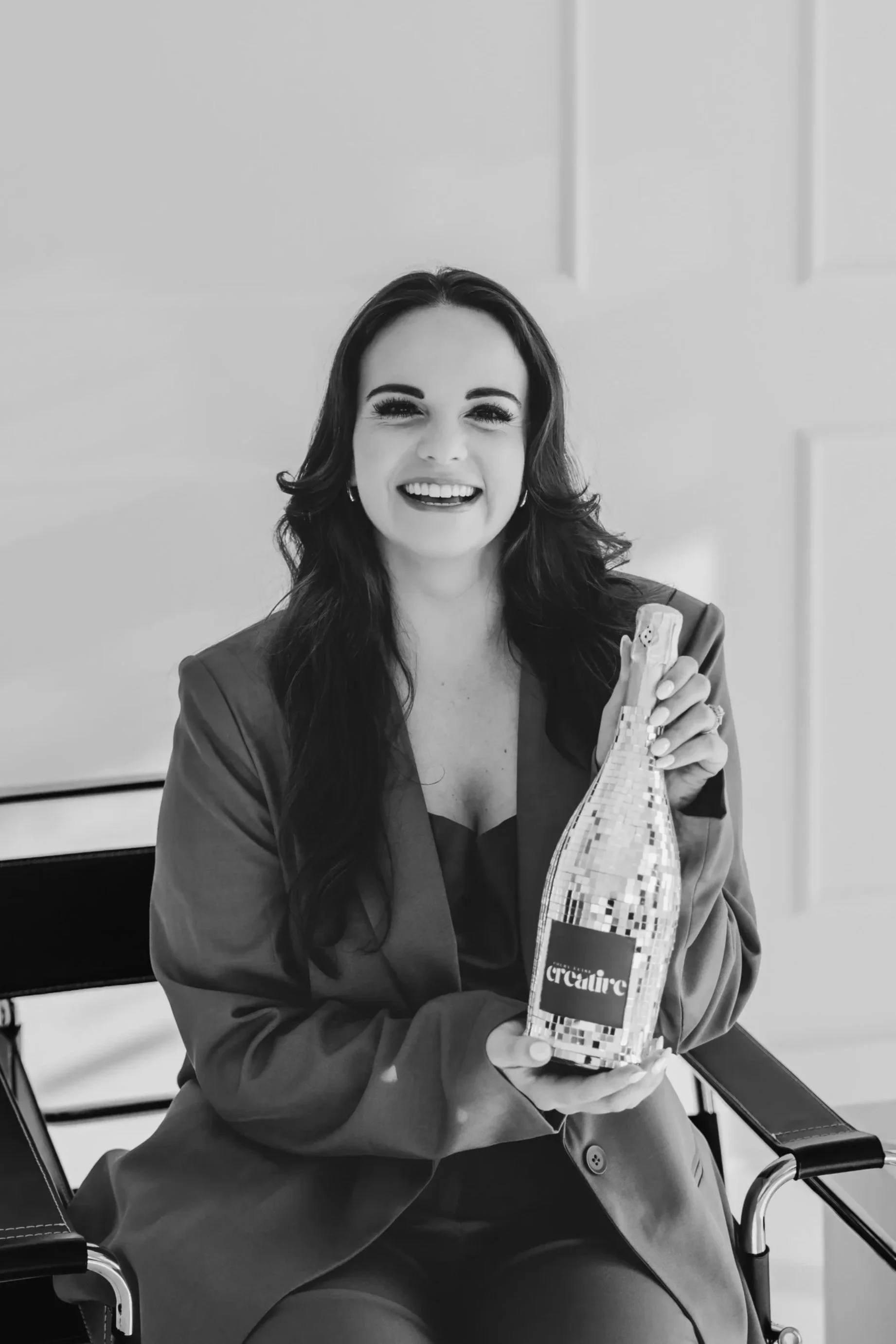Black and white image of a woman smiling and holding a disco champagne bottle