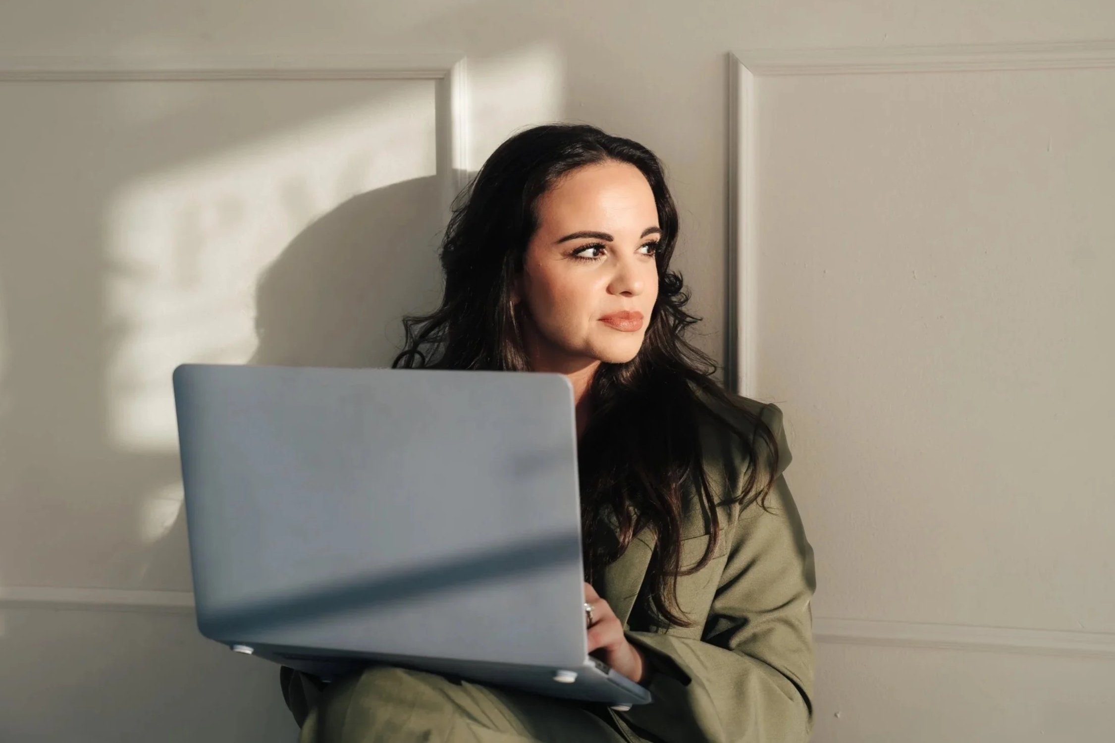 Woman in green suit holding gray laptop looks off camera