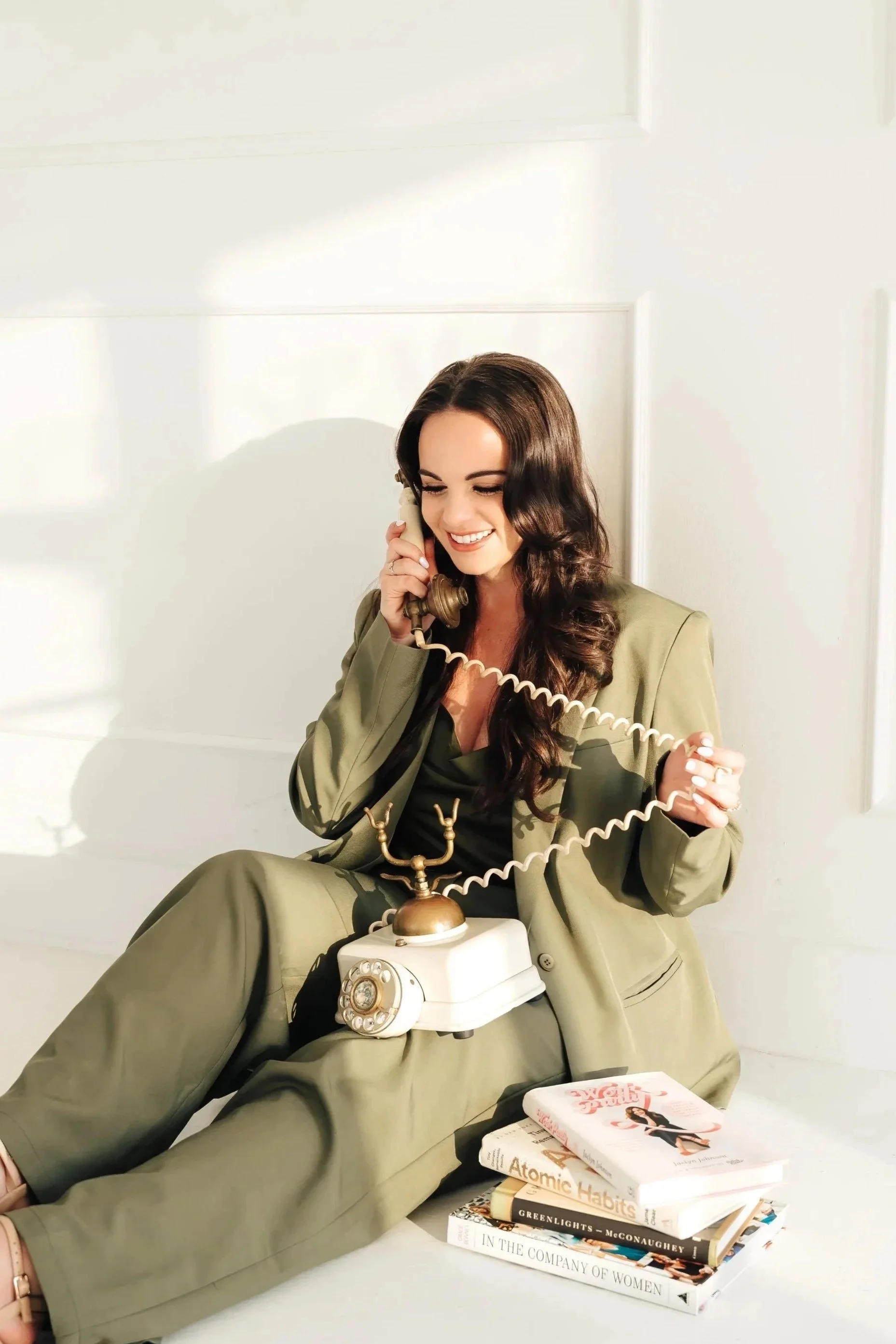 Woman in a green suit holds a rotary phone with the cord around her fingers