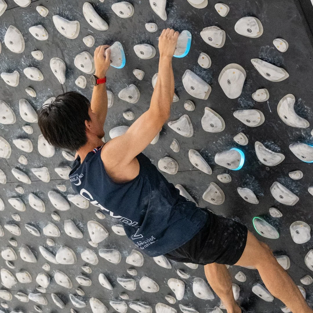 Climber on an indoor bouldering wall, reaching for holds.