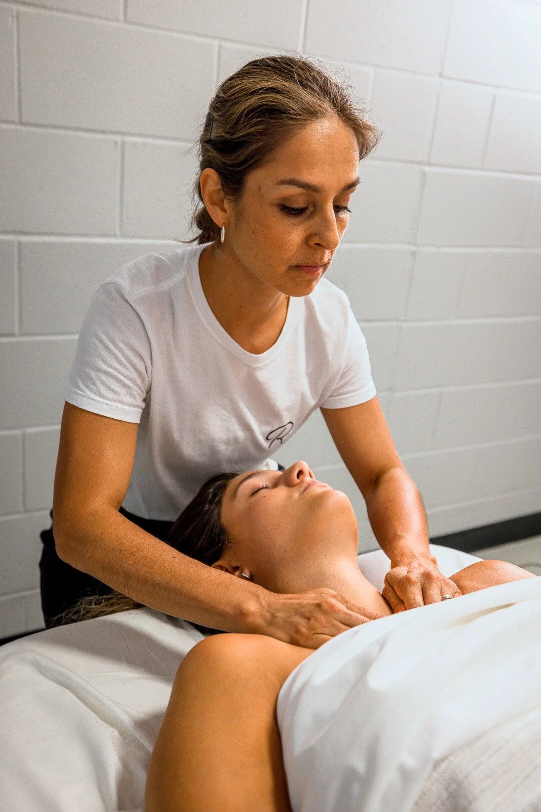 A woman receives a massage from a massage therapist in a clinical setting.