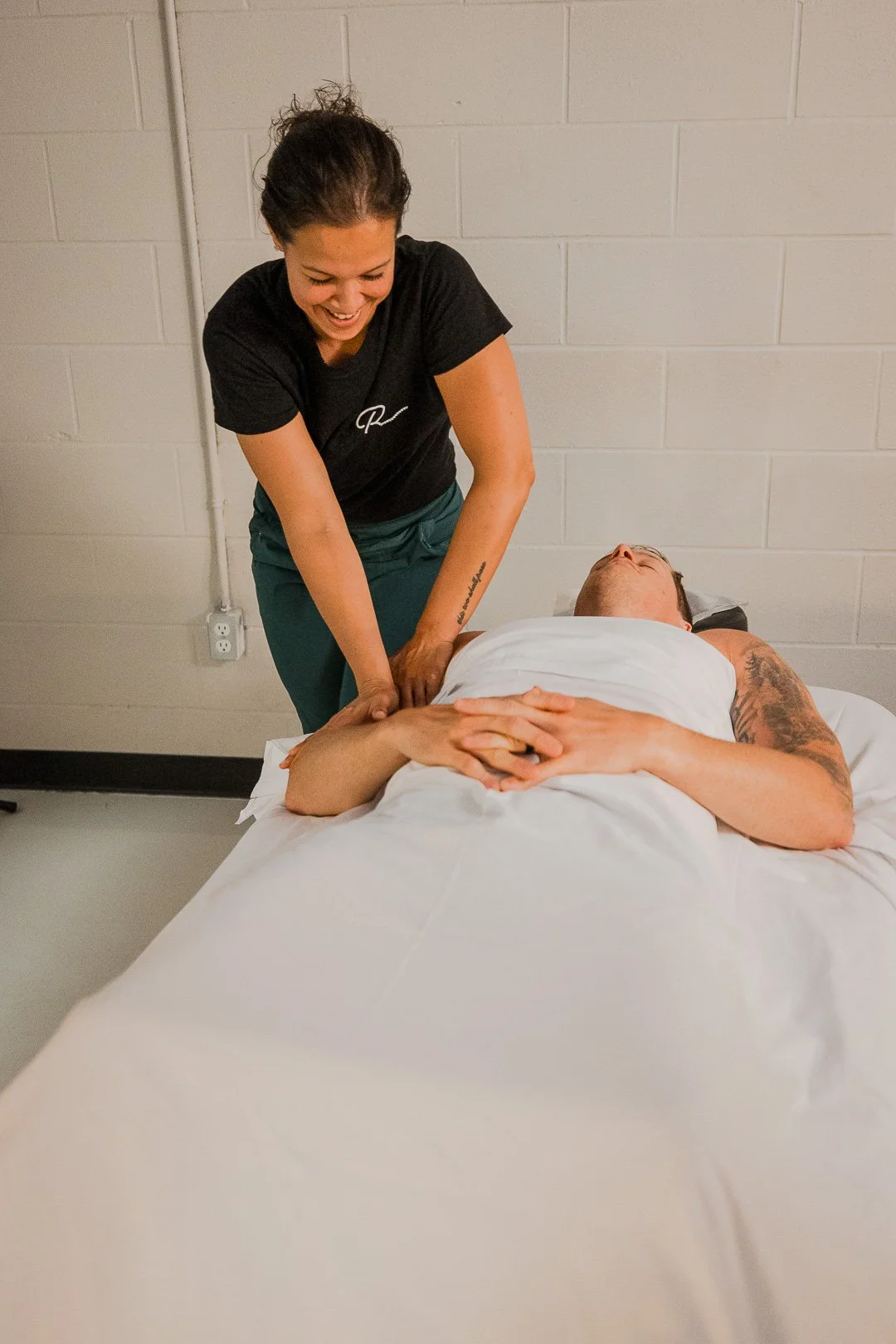 A woman giving a massage to a man lying on a bed in a clinical setting.