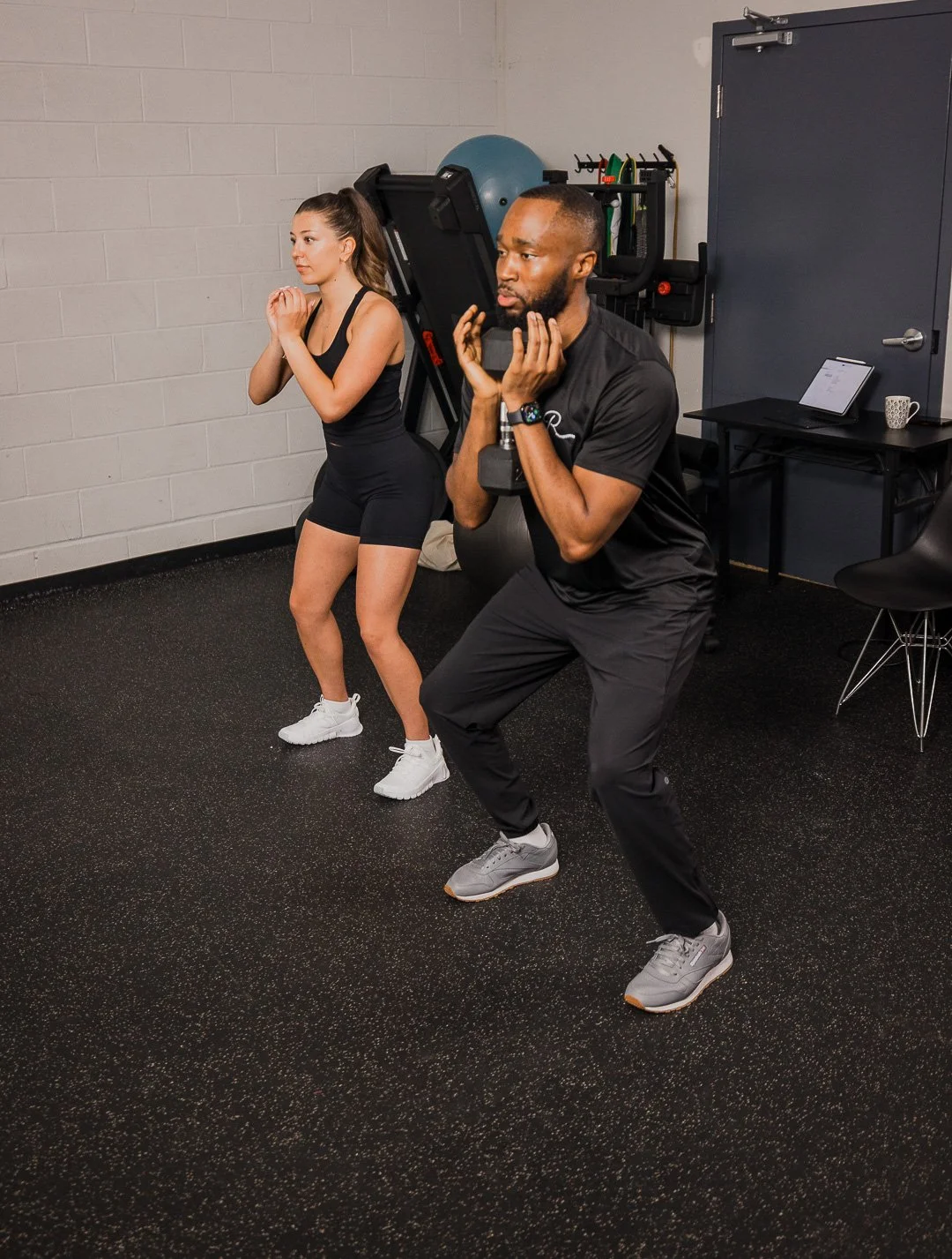 A woman doing TRX suspension training under the supervision of a physiotherapist in a gym.