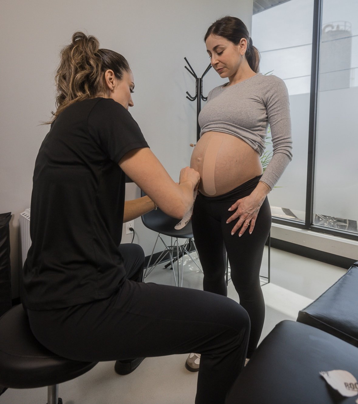 Pregnant woman getting a medical bandage applied to her belly by a healthcare professional in a clinic.