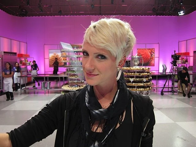 Person in a studio with purple lighting, surrounded by dessert displays and filming equipment.