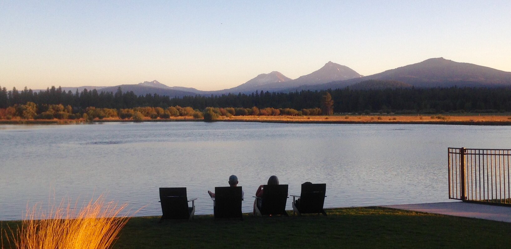 Two people sitting on chairs by the water, with mountains in the background at sunset