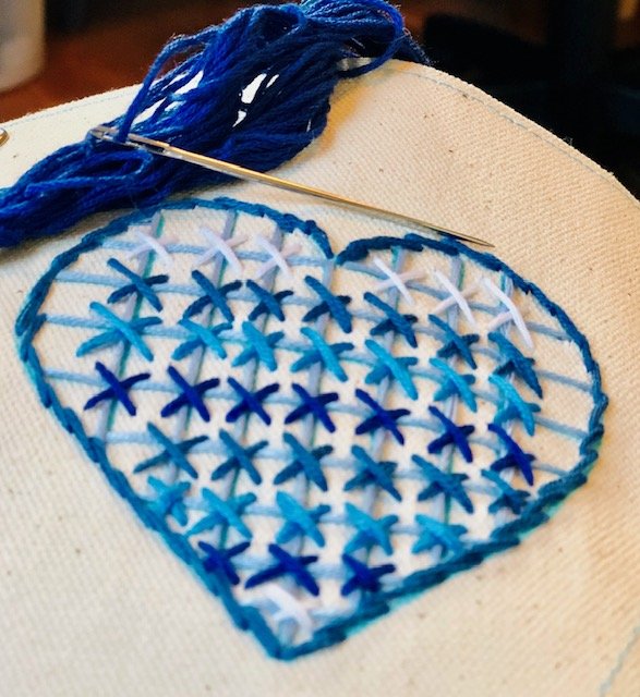 Heart-shaped embroidery pattern with blue and white star stitches and blue yarn on fabric.