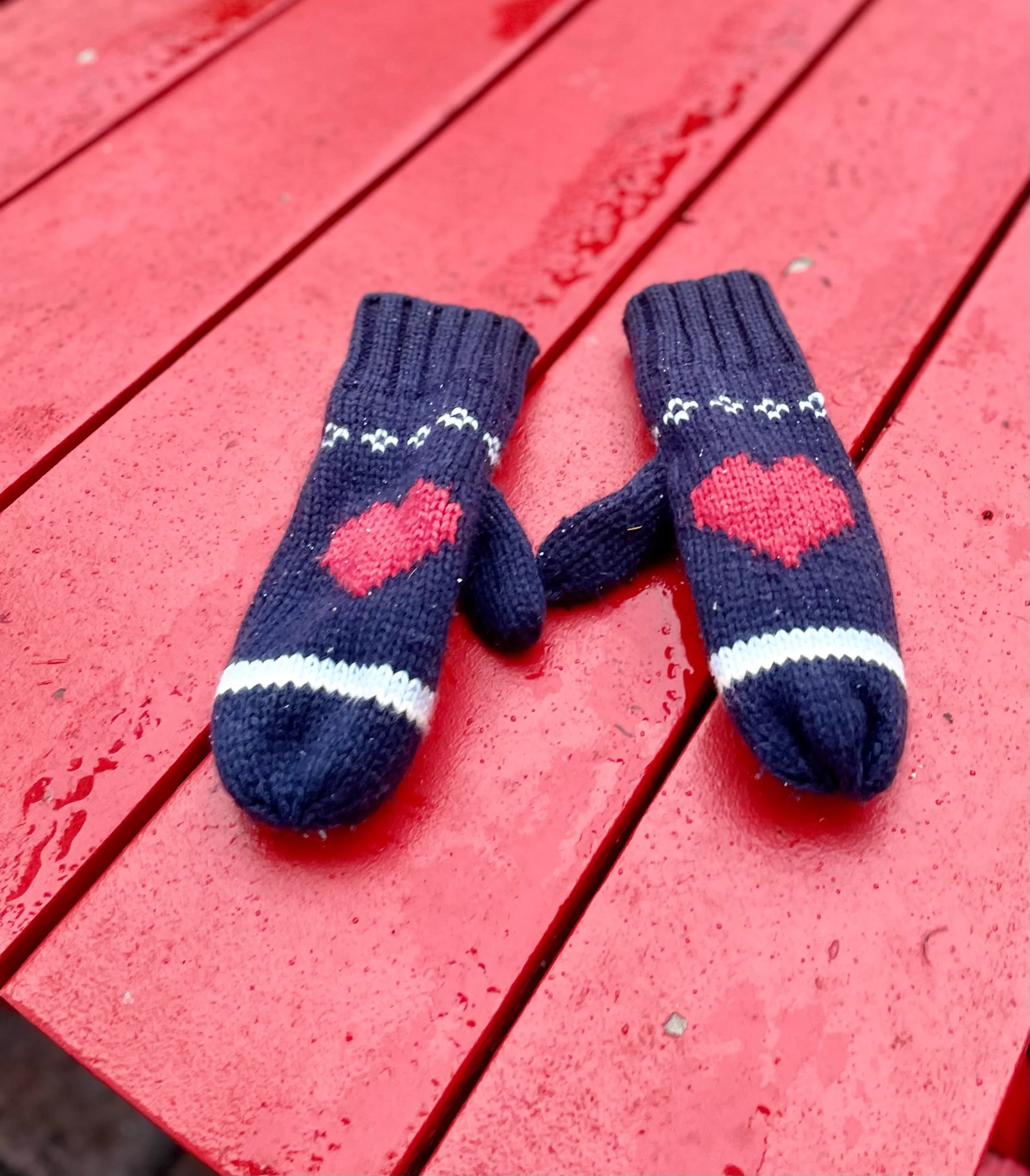 View of a person's feet wearing navy blue socks with pink hearts standing on a red wooden picnic table with water droplets on the surface.