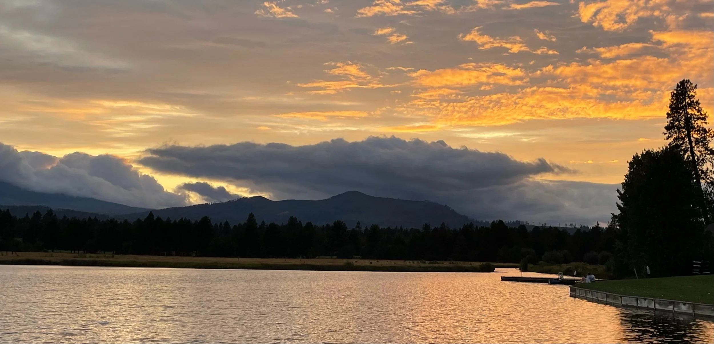Sunset over a lake with mountains in the background and trees on either side.