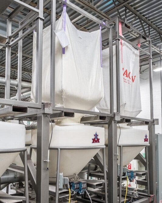 Bulk bag lifting frames are used to discharge bulk bags of raw materials into the dispensers.