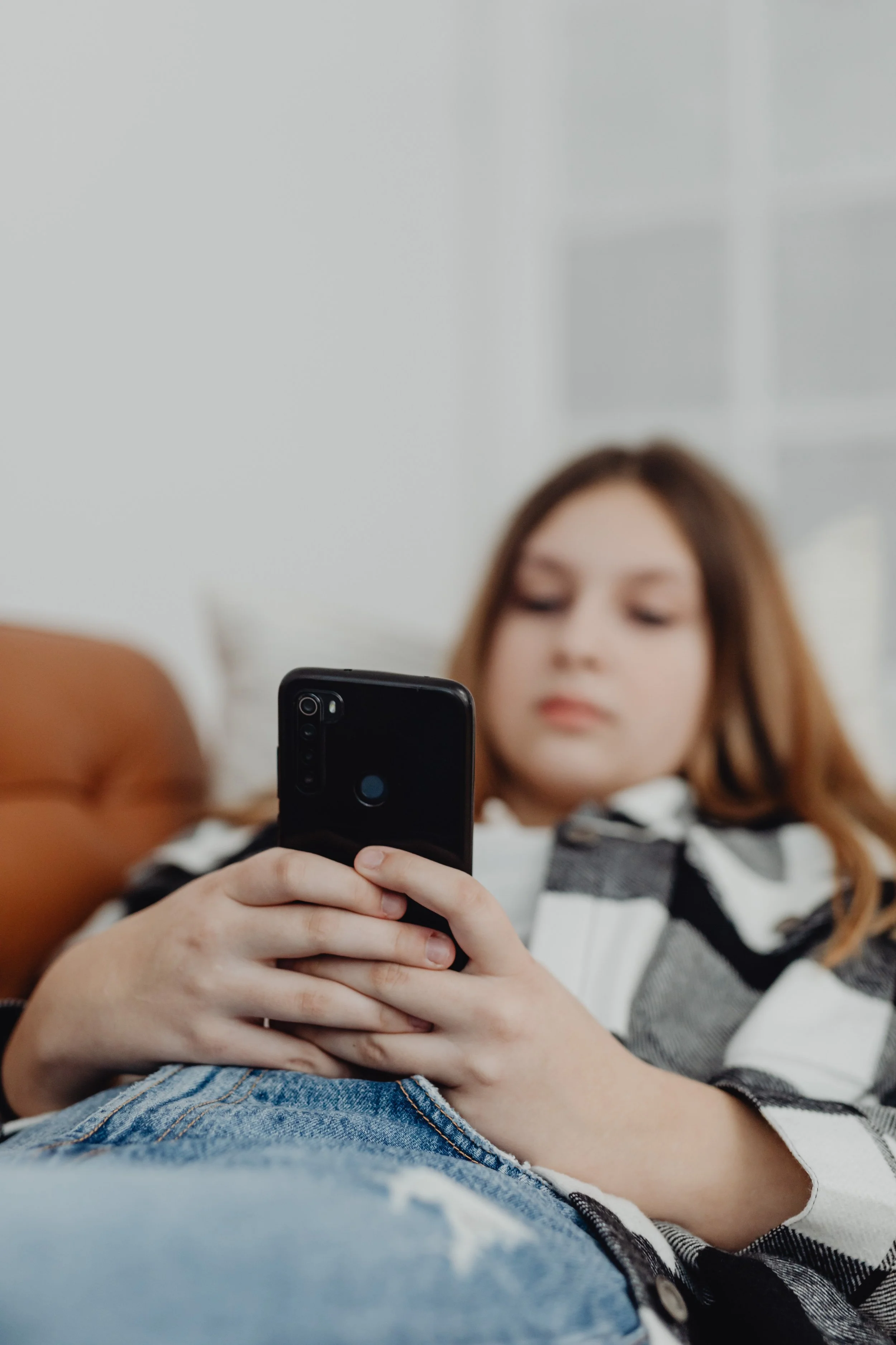 Teen lying on a couch looking at a smartphone with a neutral expression, highlighting everyday habits and screen time patterns—how to train your brain with healthier routines and the benefits of brain training.