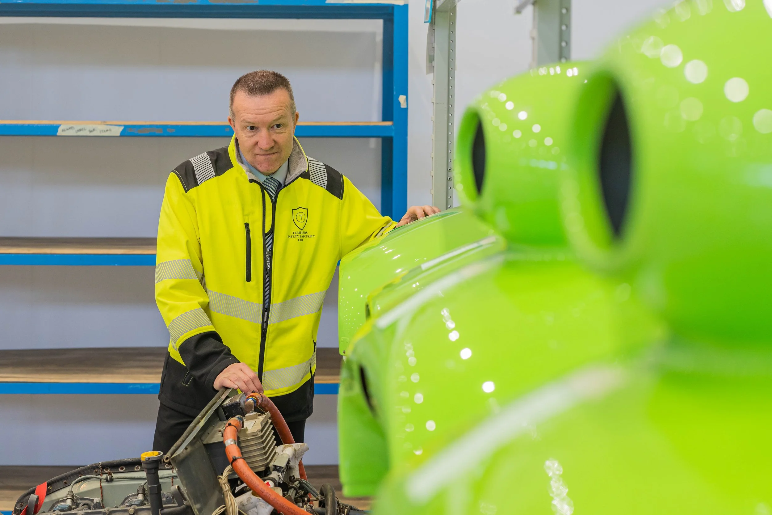 A man in a yellow safety jacket inspecting machinery in a factory or warehouse.