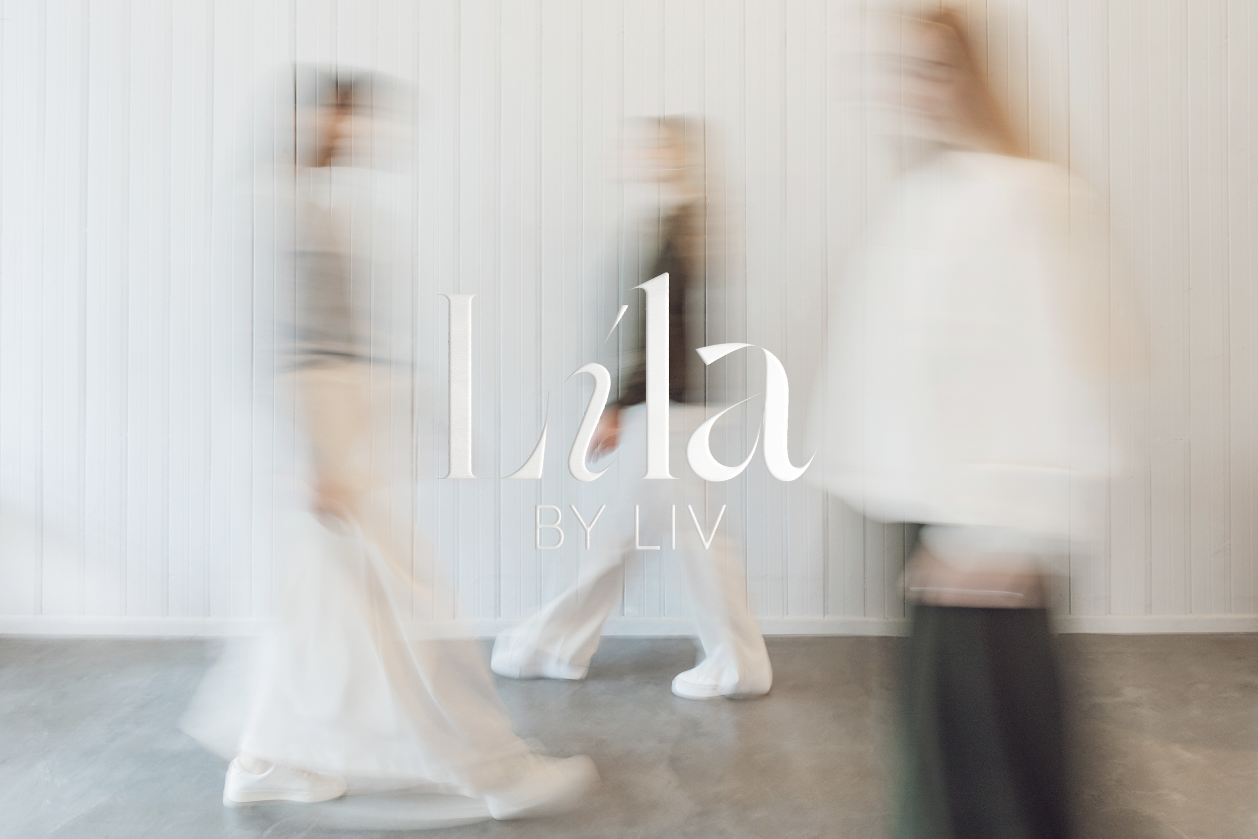 Blurred motion image of three people walking past a white wall, with the text "Líla by Liv" overlaid.