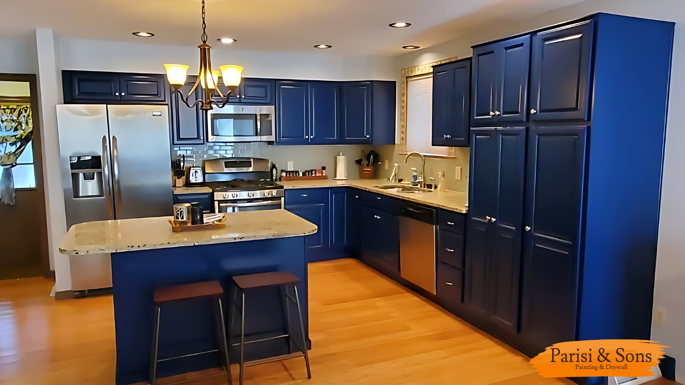 Kitchen with dark blue cabinets, stainless steel appliances, a small island with a cream-colored countertop, wooden stools, and a chandelier with five yellow-shaded lights.