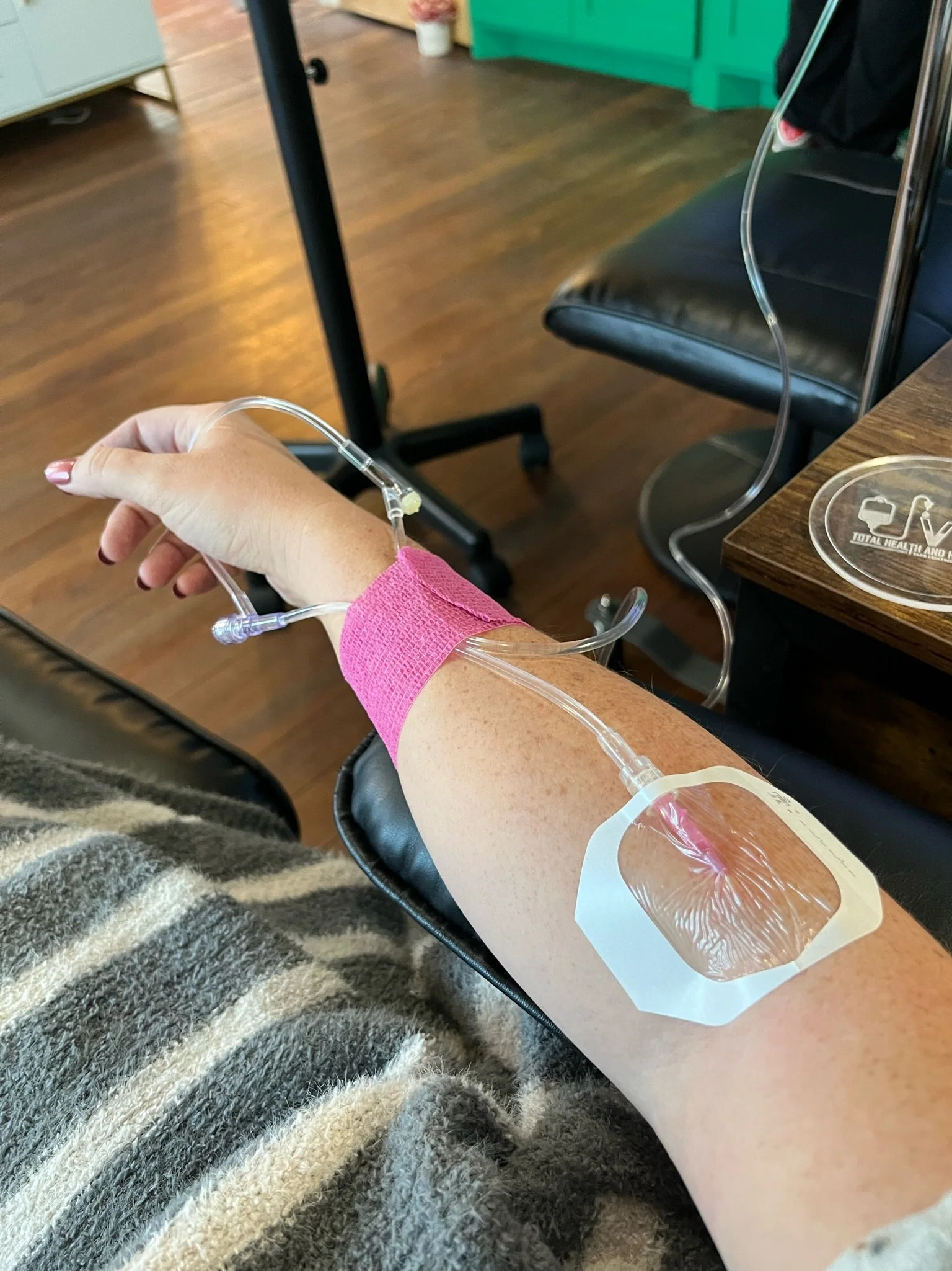A person with a striped sweater sitting in a chair with a bandaged arm drawing blood for donation. The person's arm is connected to a blood collection tube, at The Irenic Place in Aledo, Texas that used to be VIP Total Health and Hydration Aledo