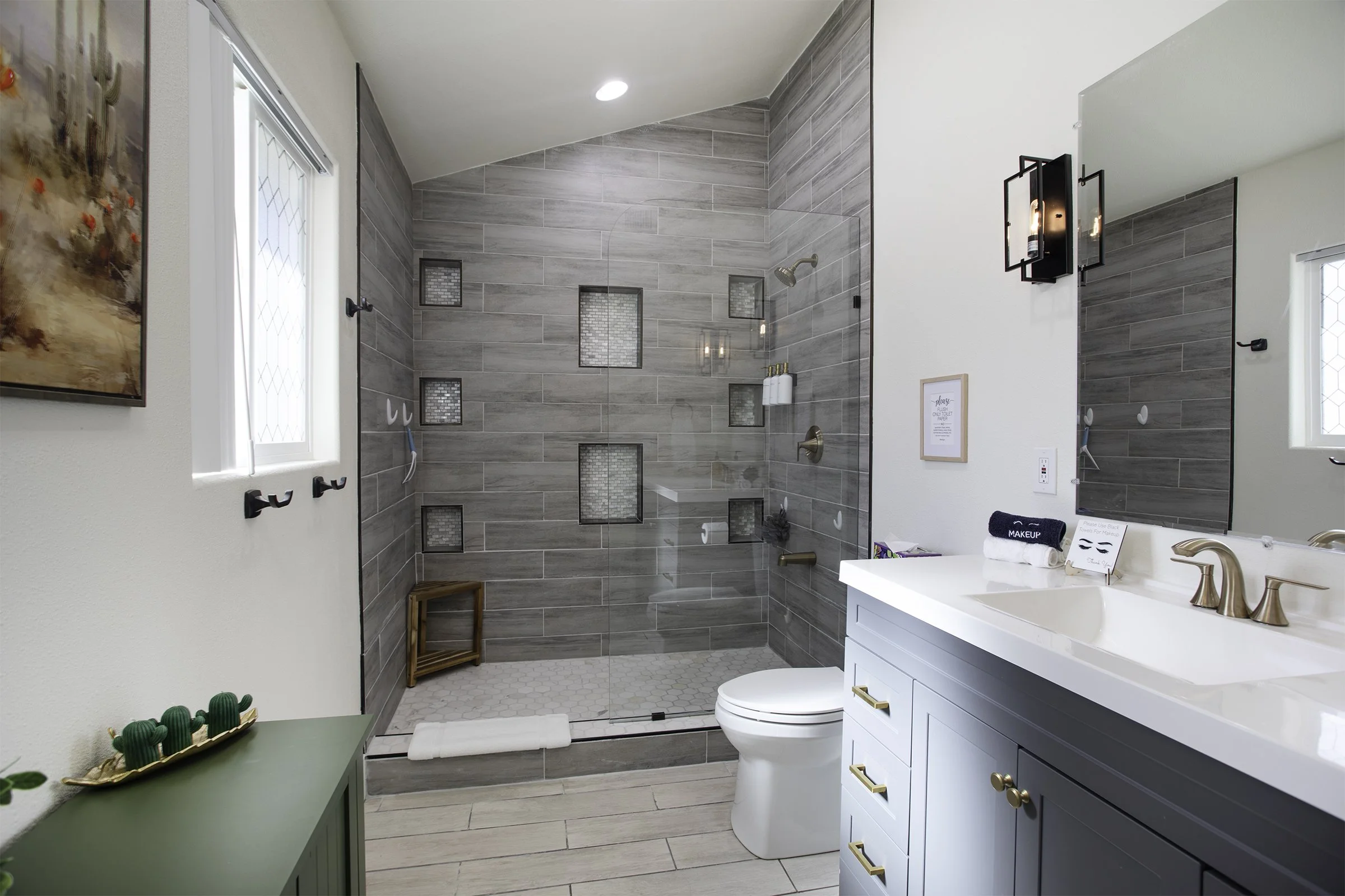 Modern bathroom with a walk-in shower, grey tile walls, and a white vanity with gold fixtures.