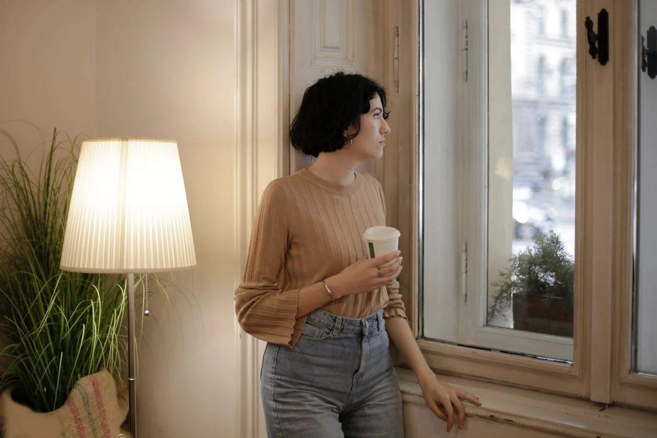 woman-in-brown-long-sleeve-shirt-and-blue-denim-jeans-holding-disposable-cup