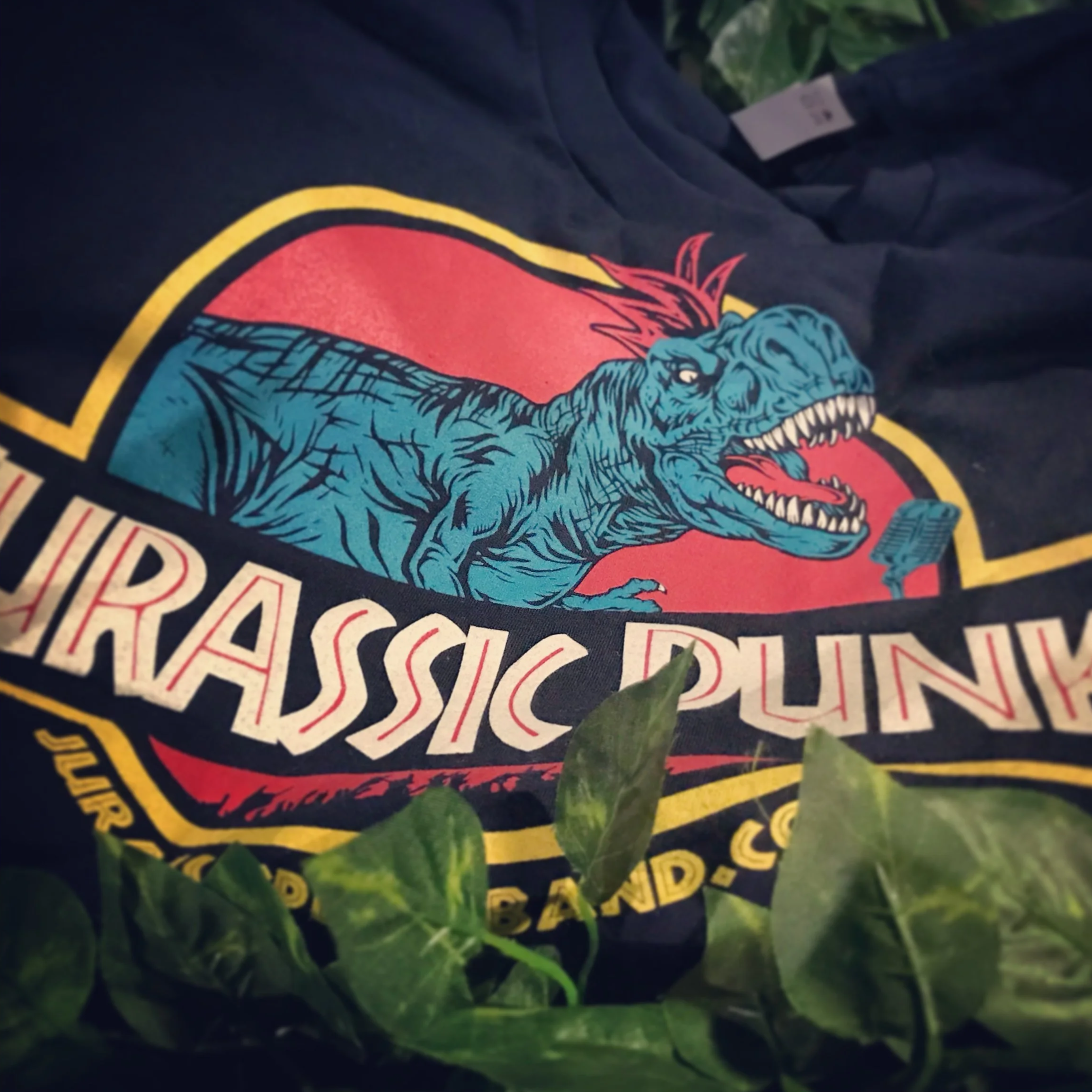T-shirt with "Jurassic Punk" logo featuring a stylized dinosaur with a mohawk, surrounded by greenery.