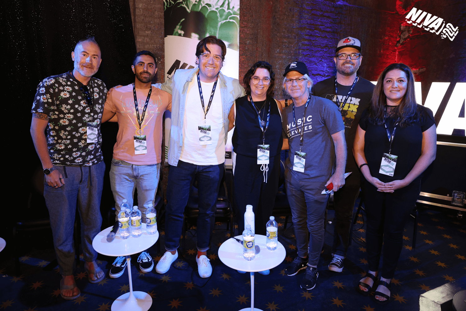 Group of seven people standing together at a conference or event, wearing badges, with a background featuring the NWAVIN logo and a dark brick wall.