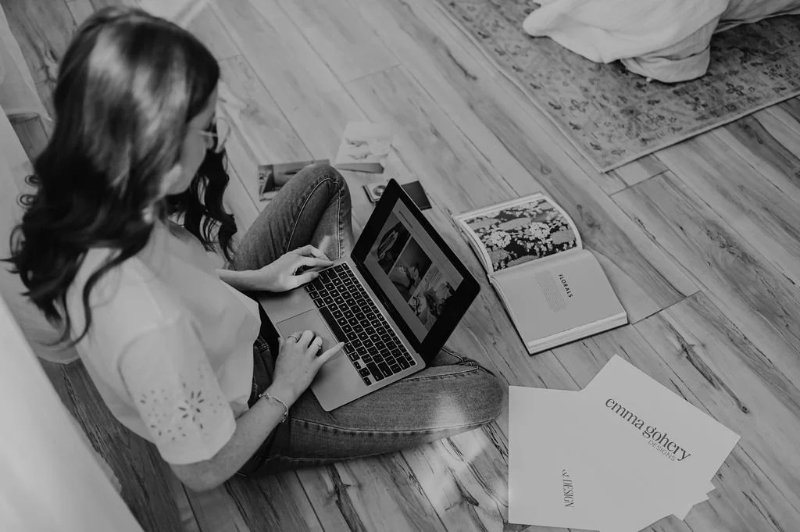 Woman sitting on floor using laptop, working on web design in Edmonton with creative tools and brand materials nearby.