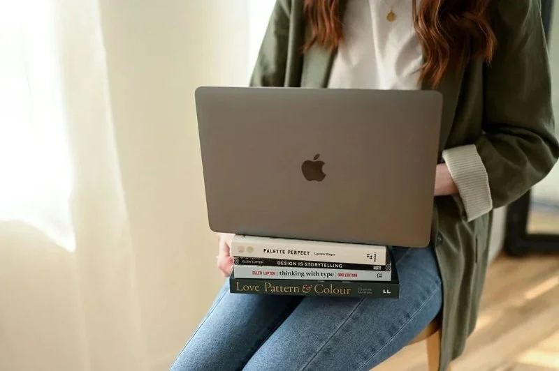 Woman working on laptop with design books, representing branding and web design strategy process.